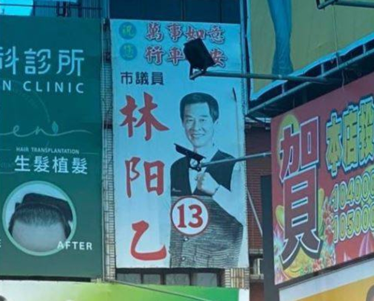 前台南市議員林阳乙在2020年的廣告看板前，就因投射燈的角度，讓不少人誤以為他拿著「手槍」。（翻攝自新·路上觀察學院）