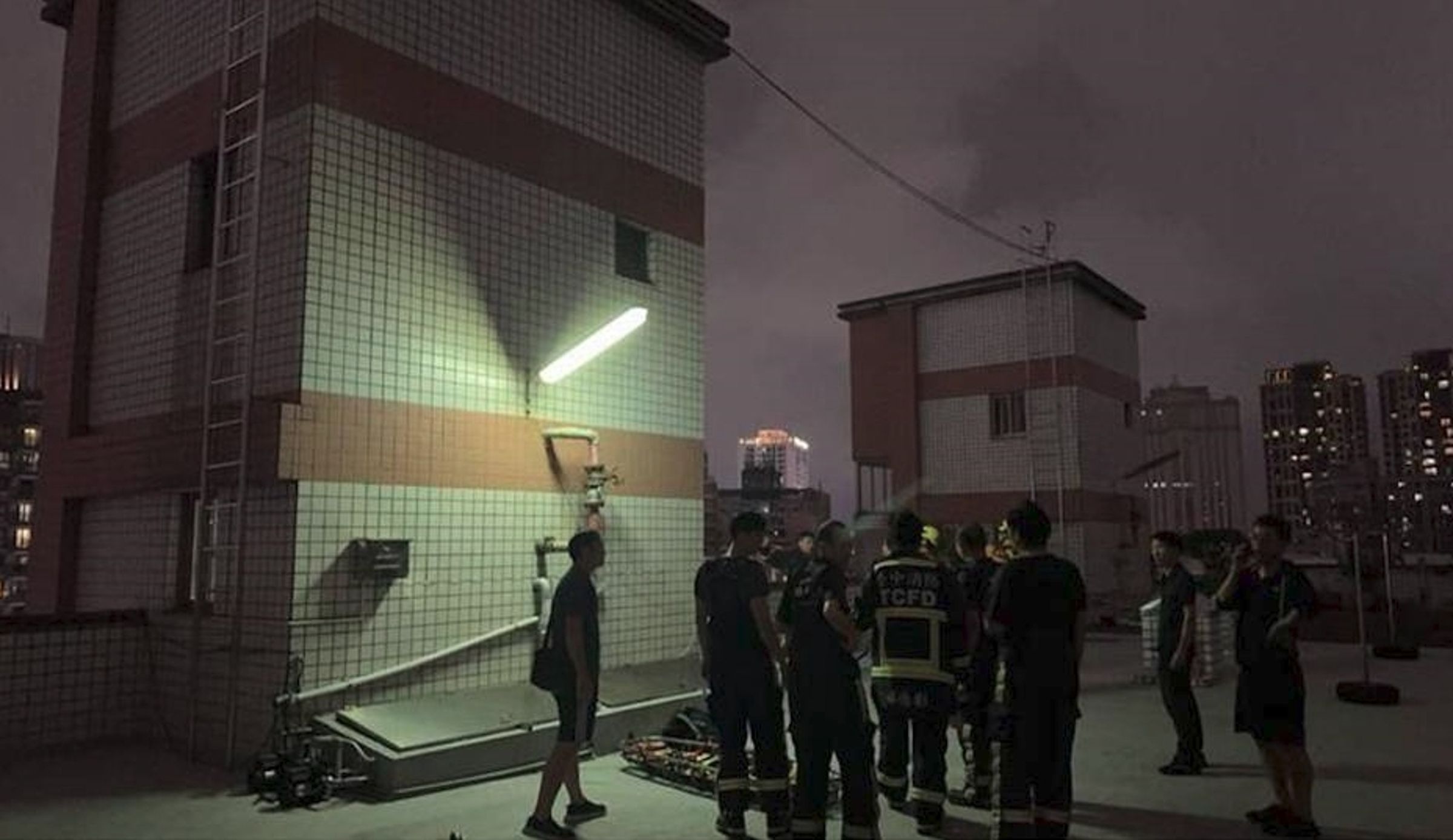 台中一社區大樓頂樓水塔驚見男子陳屍,搜救隊在閃電與雨勢中進行吊掛作業。(翻攝畫面)
