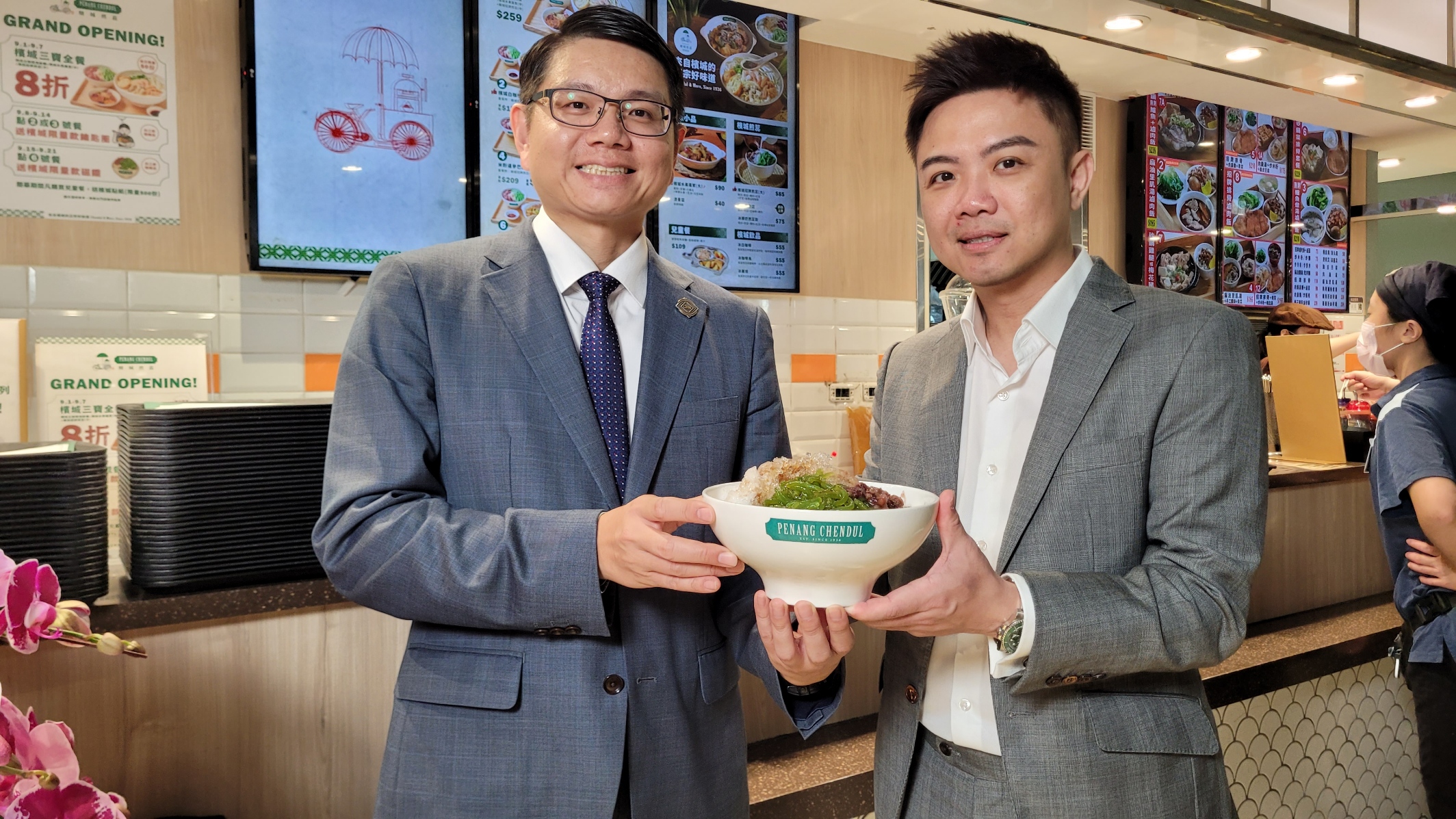 揚秦董事長卓靖倫（左）和馬來西亞檳城煎蕊總部執行長張文華（右），手捧檳城煎蕊的招牌菜「煎蕊」，這是在刨冰淋上椰奶、糖漿，搭配紅豆、斑蘭葉汁粉條等配料的特色甜點。
