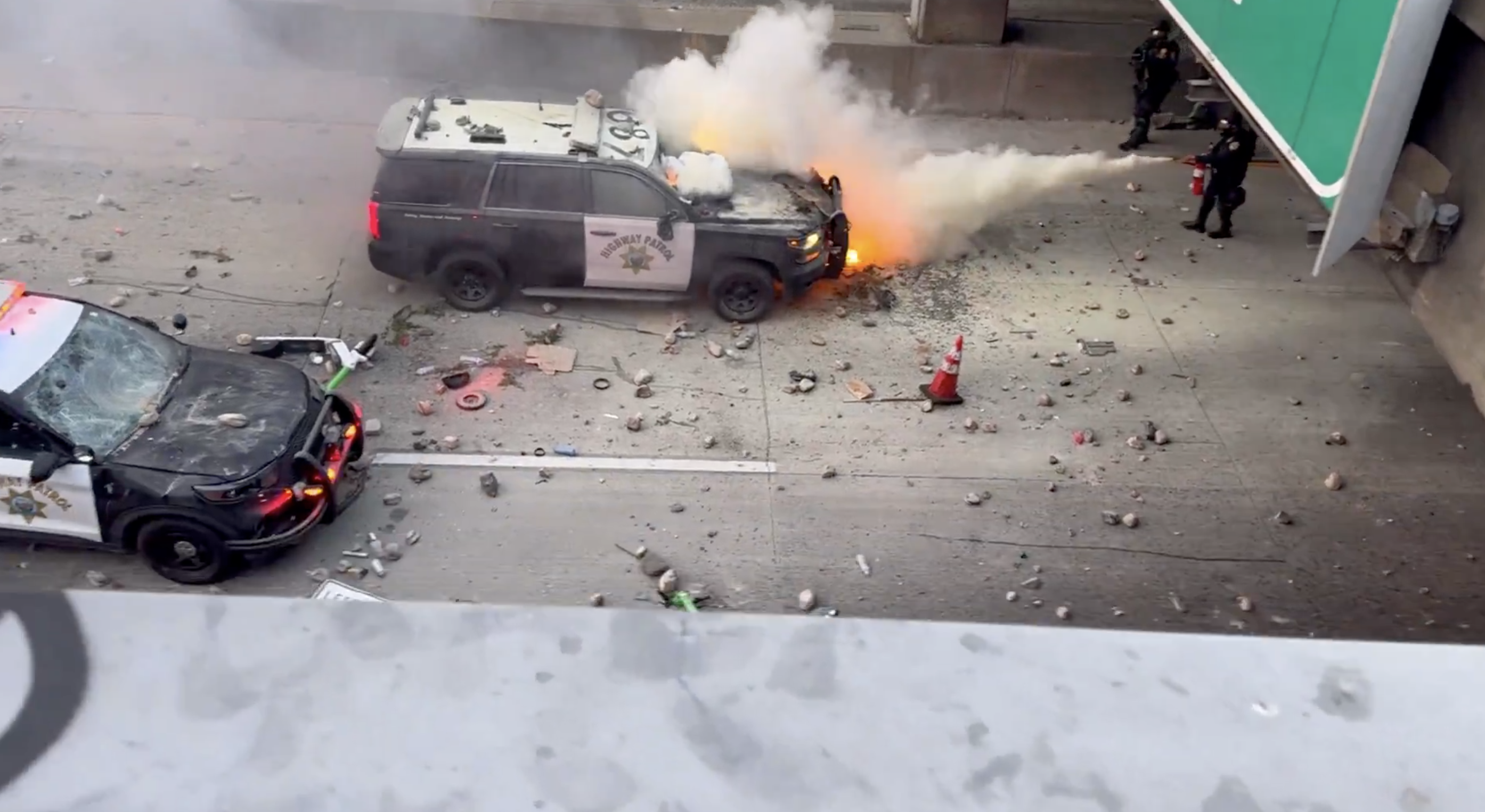 洛杉磯抗議民眾點燃物品並從天橋上扔下，導致一輛警車起火燃燒。（翻攝自X@CollinRugg）