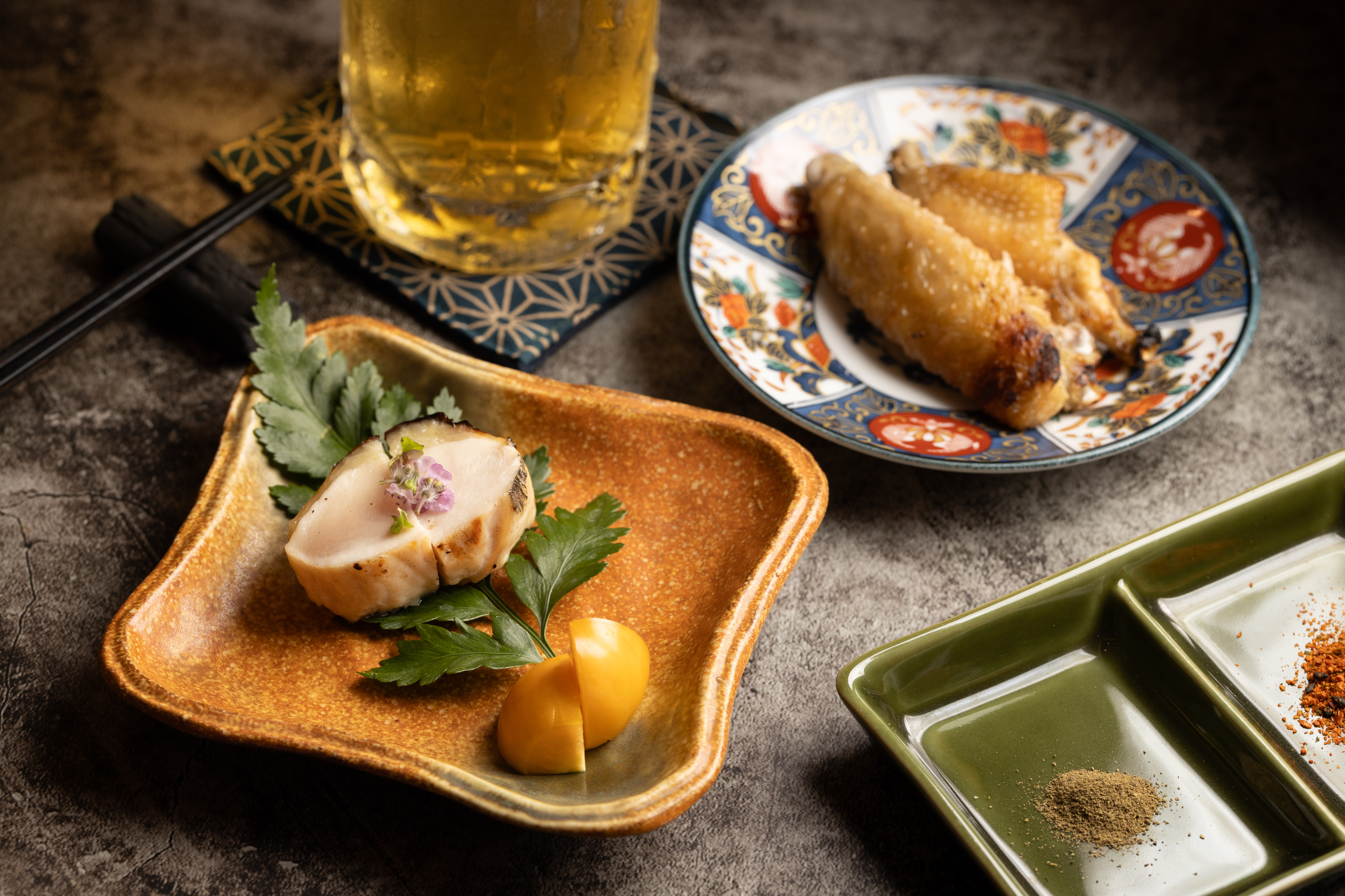 以魚料理常使用的西京燒手法製作「雞胸西京燒」(左前)醃漬6小時入味後,再以炭火燒烤;「雞翅手羽先」(右後)除了強化煙燻香氣外,再刷上山椒油提昇香氣。(3,800元套餐菜色)