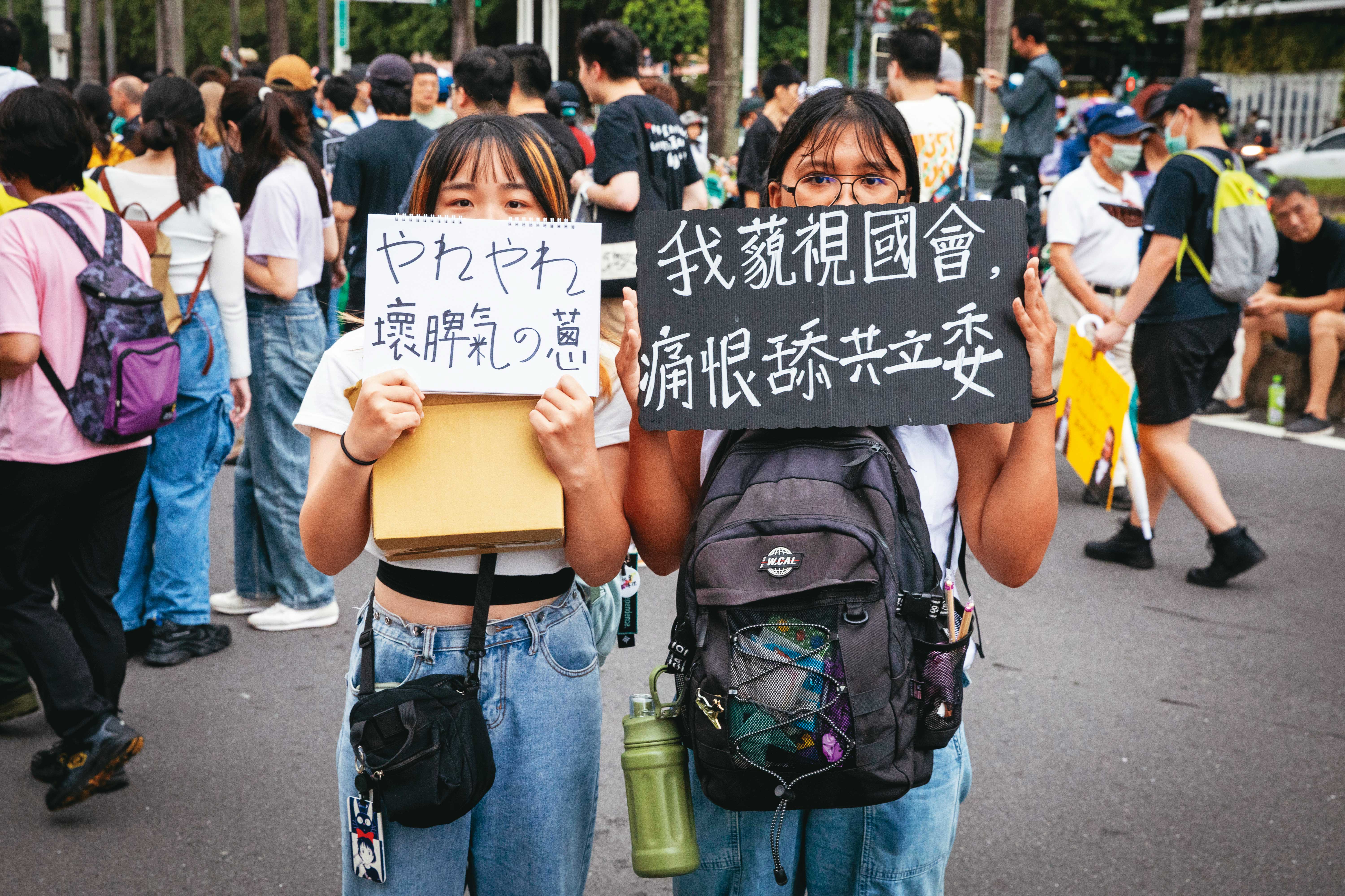 在課金組的支持下，追星族小真（左）特地從花蓮北上，第一次參加街頭運動，她舉的標語「呀勒呀勒壞脾氣的蔥」改編自洗腦神曲〈晚安大小姐〉，抗議強推法案的立委黃國昌。