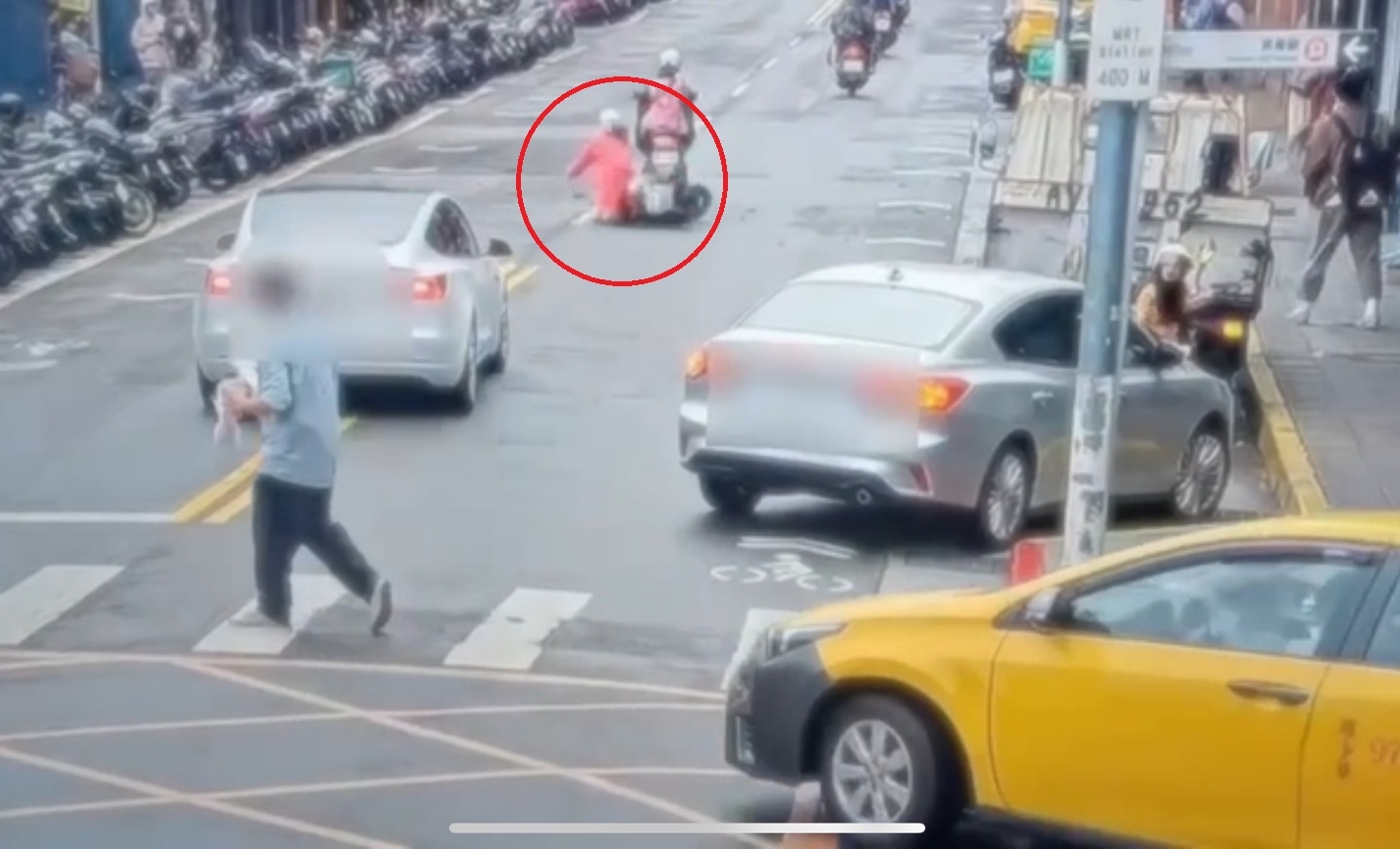 黃女（紅圈）行經該路段時，恰巧碰上大樓外牆磁磚脫落而打滑摔車。（翻攝畫面）