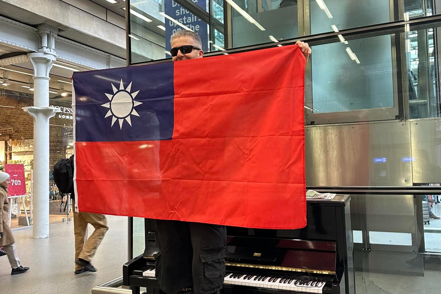 英國鋼琴家卡瓦納在倫敦聖潘克拉斯車站高舉中華民國國旗。（翻攝自Dr K Boogie Woogie臉書）