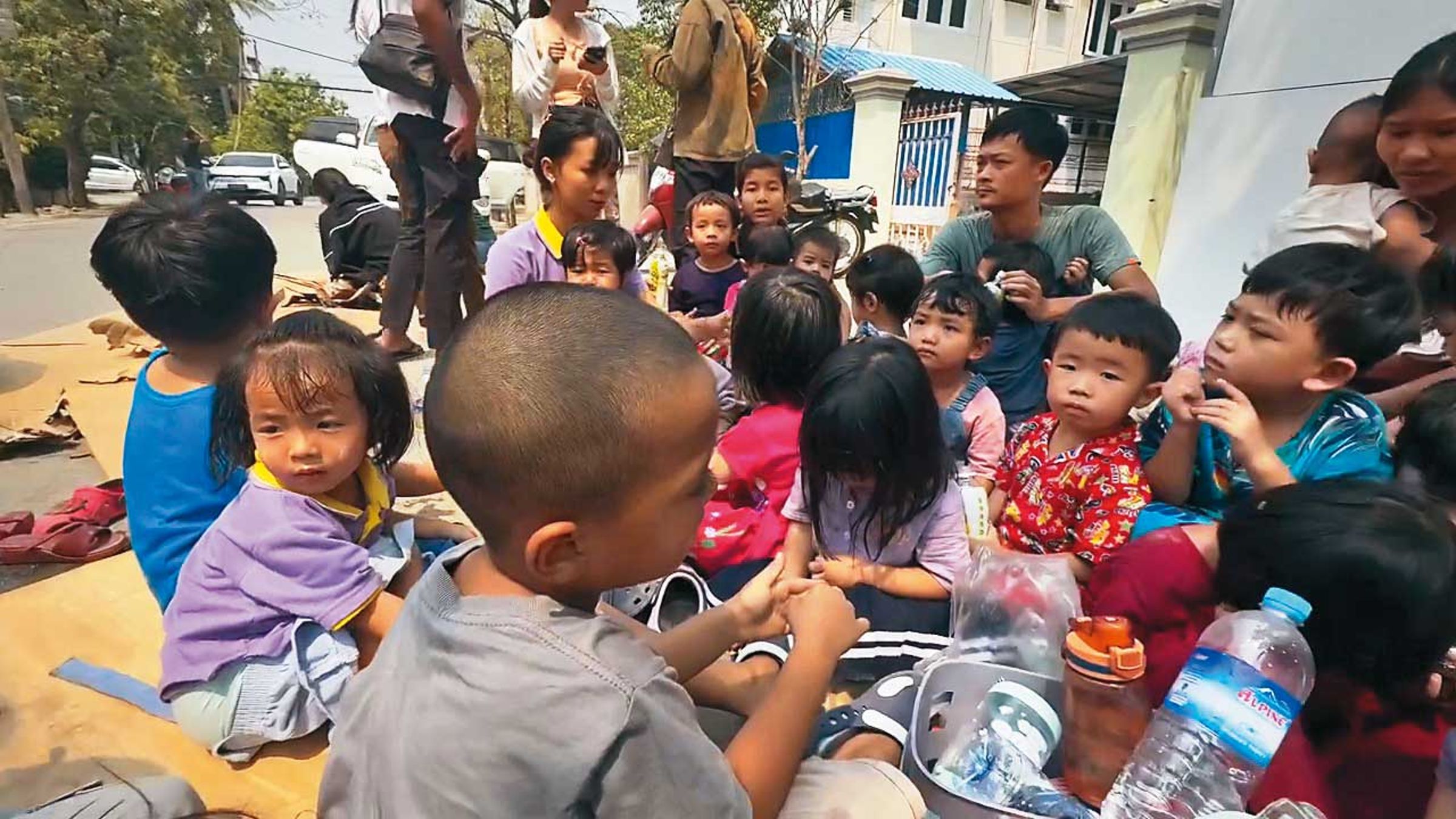 強震發生後,在大人引導下,一群緬甸孩童躲到戶外避難。(翻攝畫面)