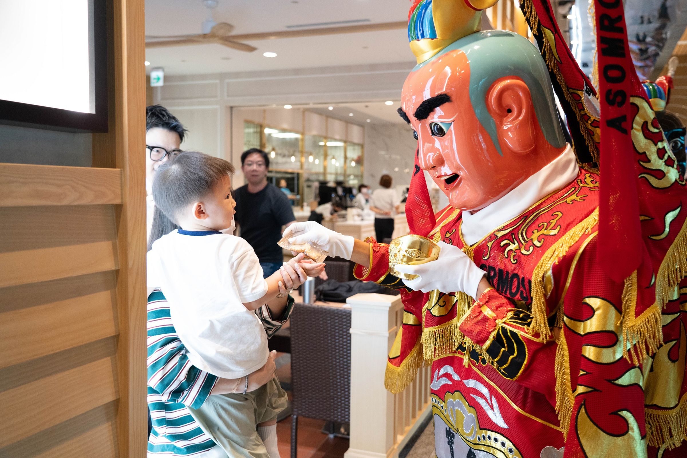 三太子現身機場，向小朋友遞上象徵吉祥的金元寶，讓旅程從祝福開始。（財團法人昇恒昌基金會提供）