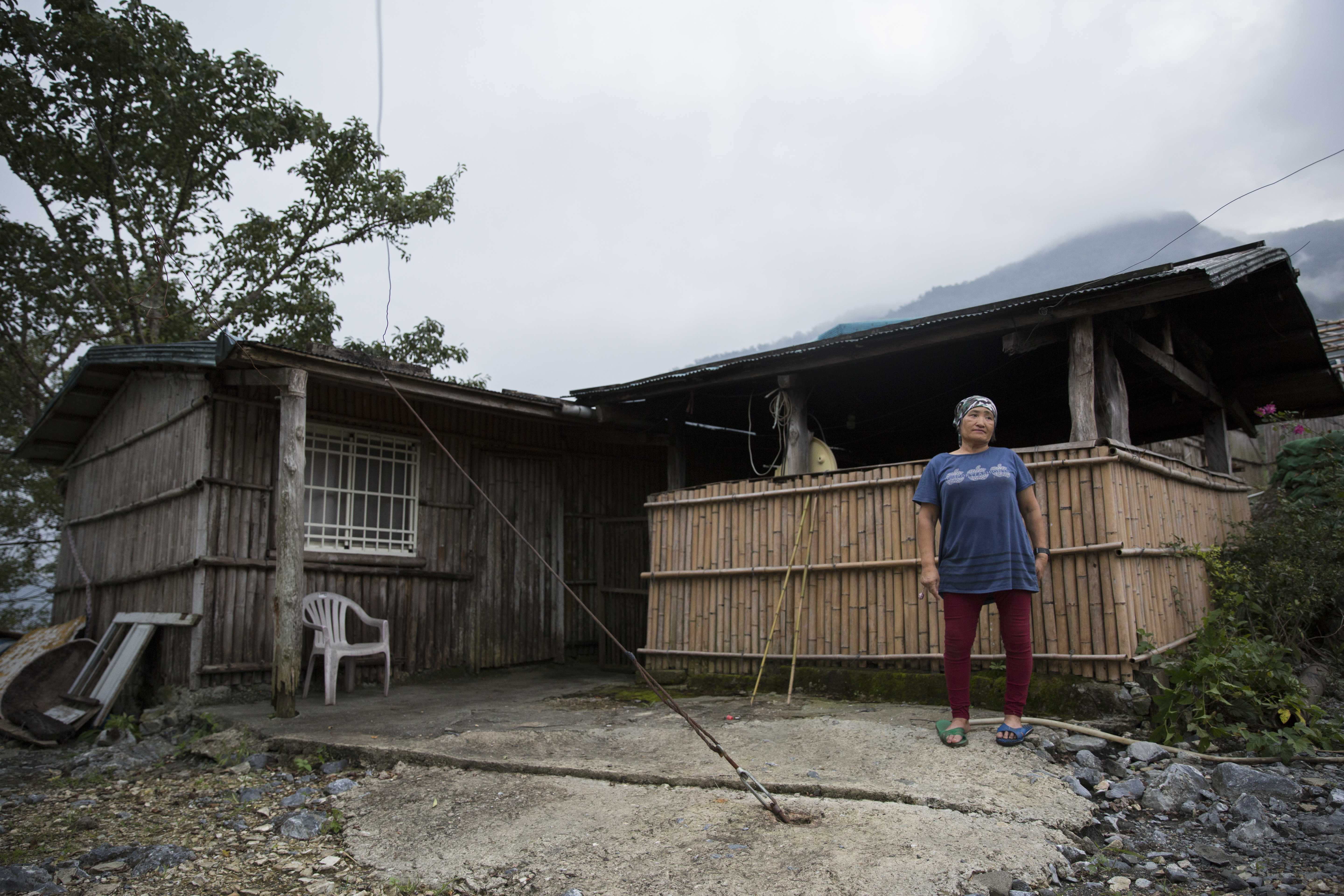 洛金的乾媽Aput站在大同部落的住家前，曾經遭逢祝融的住家已重新搭建，如今太陽能供電提供了更安全潔淨的照明。