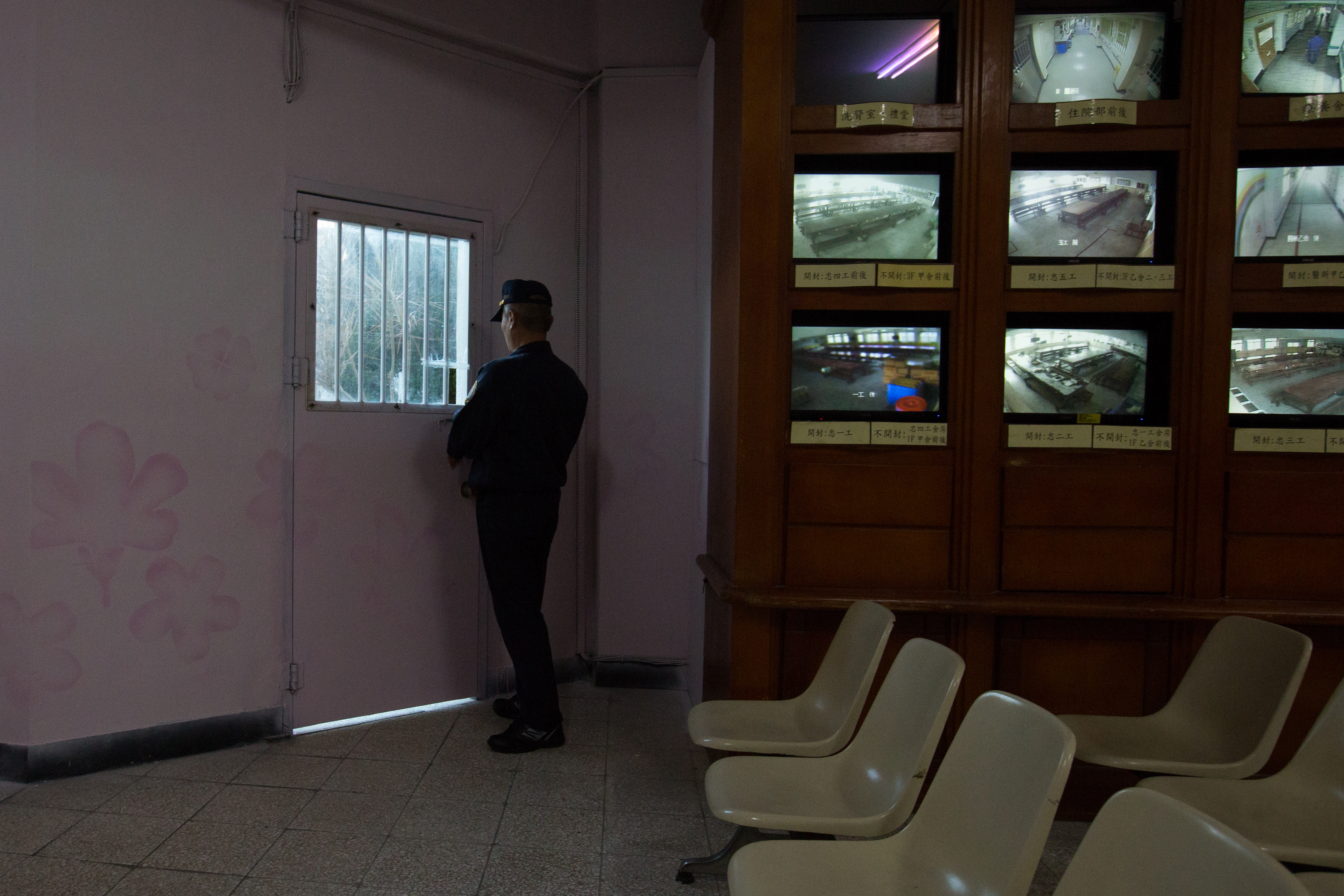 管理員鎖上囚室外公共區域的小門，一旁是監控台前的監視器電視牆。