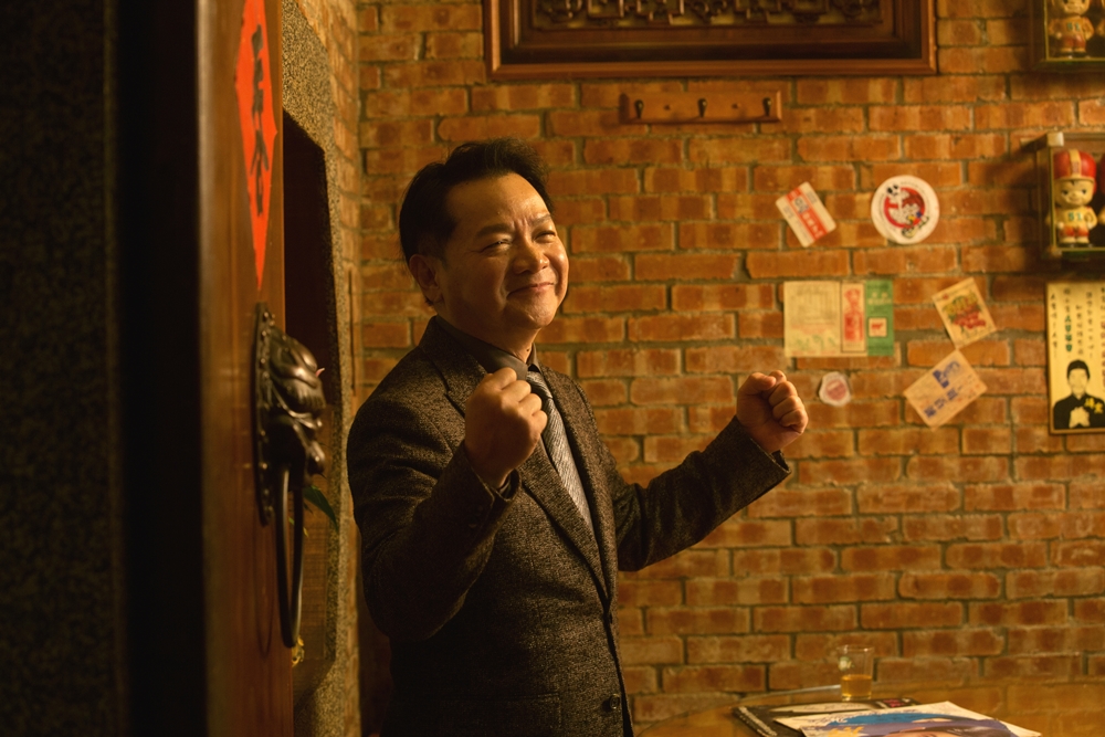 葉啟田西裝筆挺站在紅磚厝內，宛若少年時衣錦返鄉的模樣。