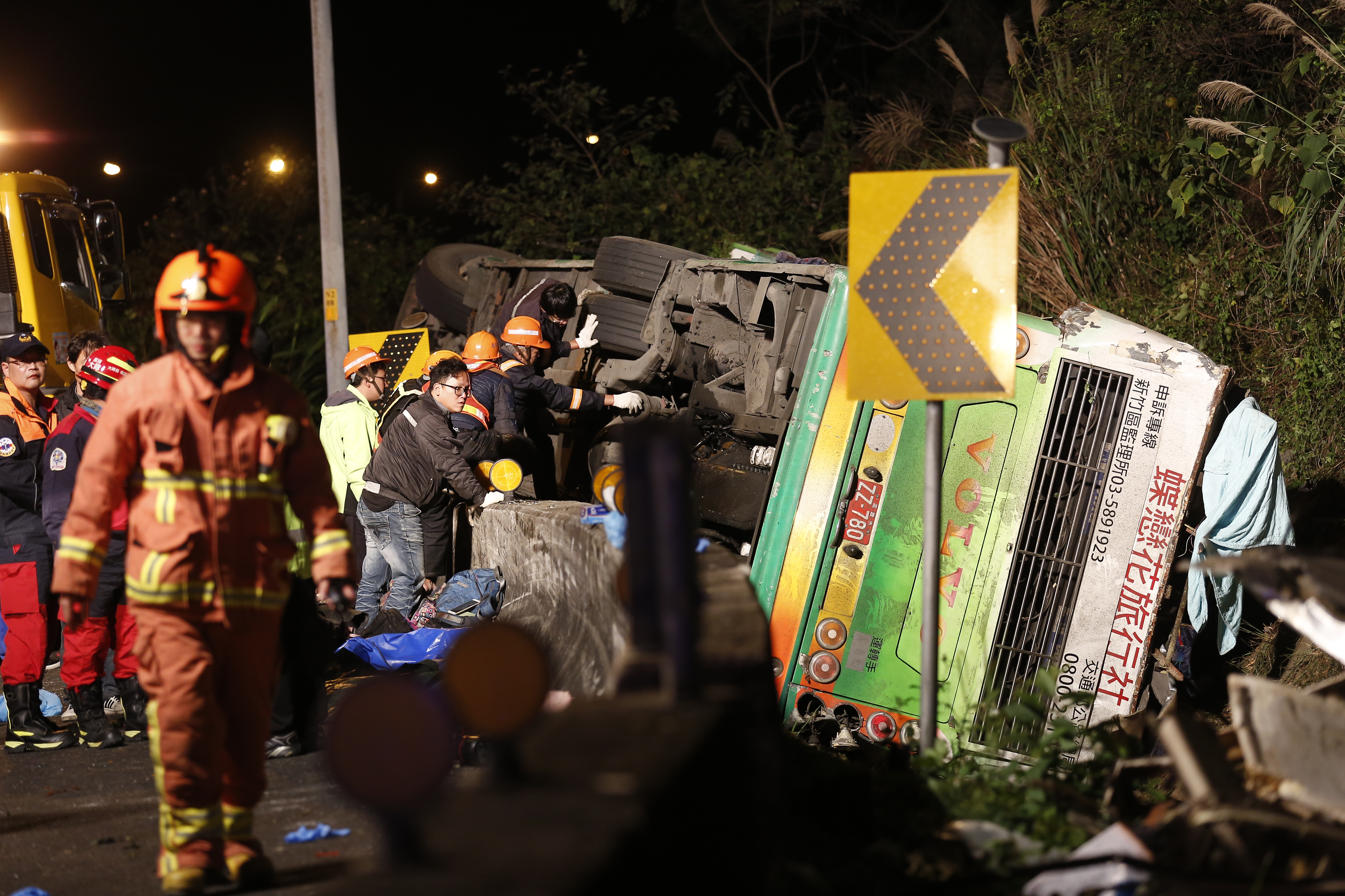 警消在遊覽車翻覆的邊坡仔細搜尋，由於車門被車身壓著，也增加施救難度。