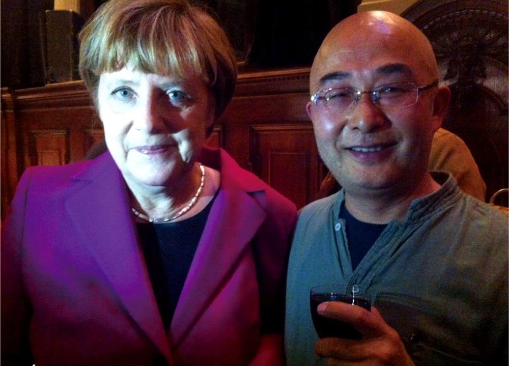 2014年,廖亦武(右)在柏林圍牆倒塌25週年音樂會和德國總理梅克爾(左)聊天,他滿臉通紅,已有醉意。(廖亦武提供)