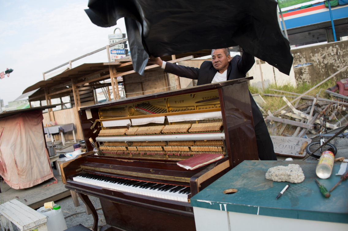 鋼琴用塑膠布蓋著，彈奏前掀開，像是打開了音樂廳布幕。