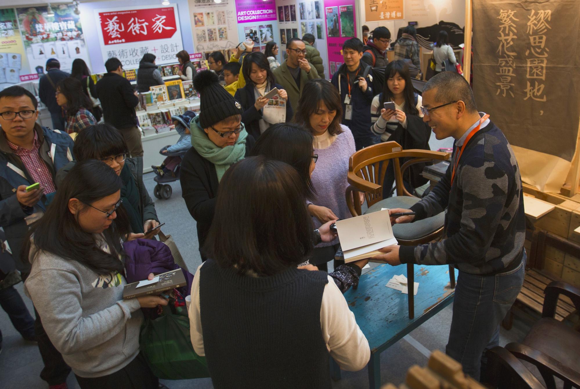 畢飛宇(右一)受邀台北國際書展座談,會後排滿了簽書粉絲,但因為去年脊椎才剛開完刀,無法久坐,簽累了,他索性把凳子疊到桌上,站著簽。