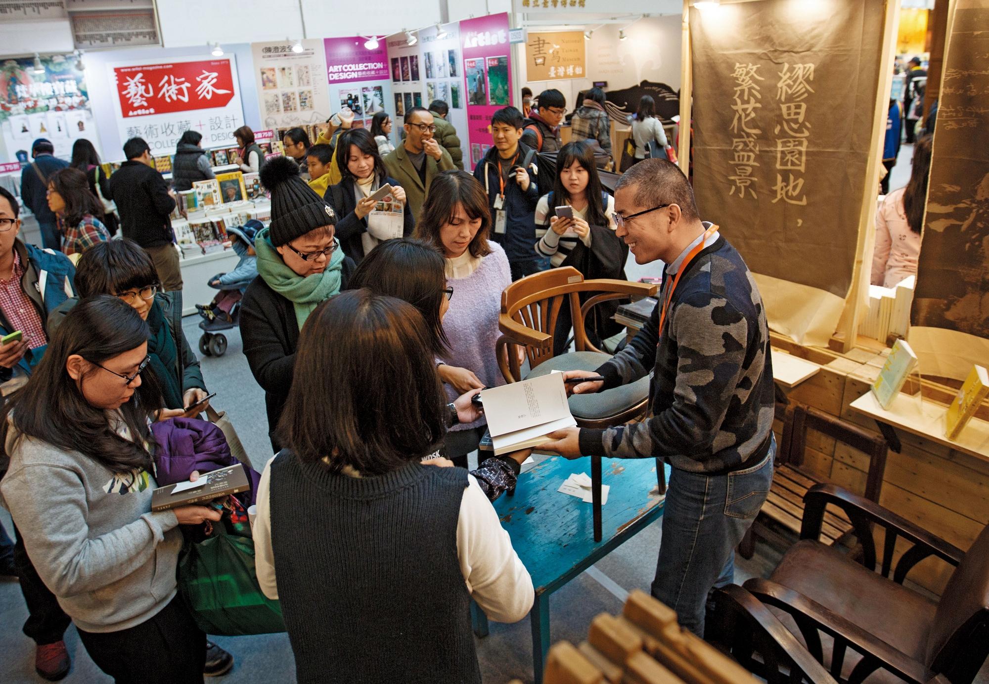 畢飛宇(右一)受邀台北國際書展座談,會後排滿了簽書粉絲,但因為去年脊椎才剛開完刀,無法久坐,簽累了,他索性把凳子疊到桌上,站著簽。