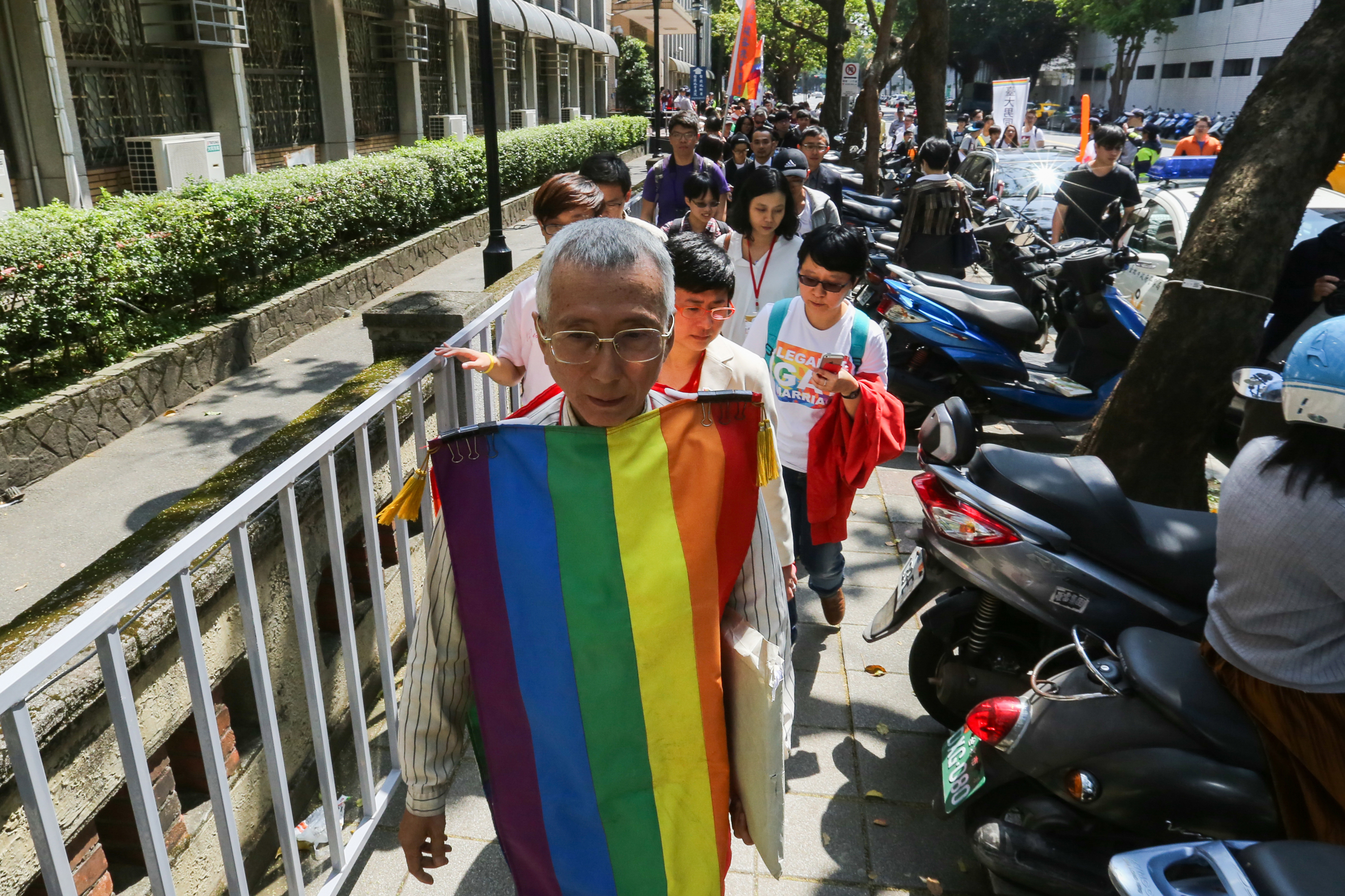 祁家威再次披上彩虹旗，在支持者陪同下走在司法院旁的人行道上。