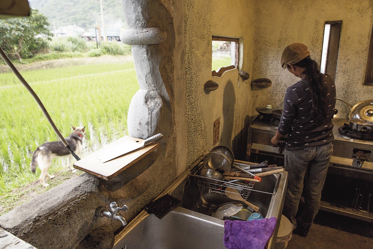 舒米.如妮在自行設計建造的小屋廚房裡燒菜,窗戶洞開沒有紗窗,望出去便是綠油油的稻田,偶爾有貓跳上跳下。