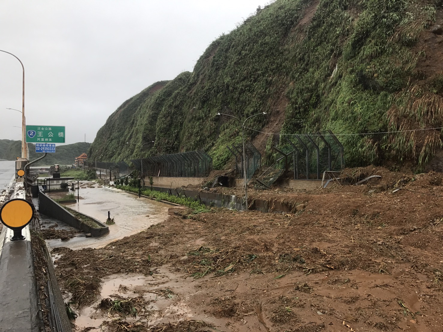 暴雨來襲，淡金公路上的滾滾泥流將路旁的鐵柵欄沖毀。