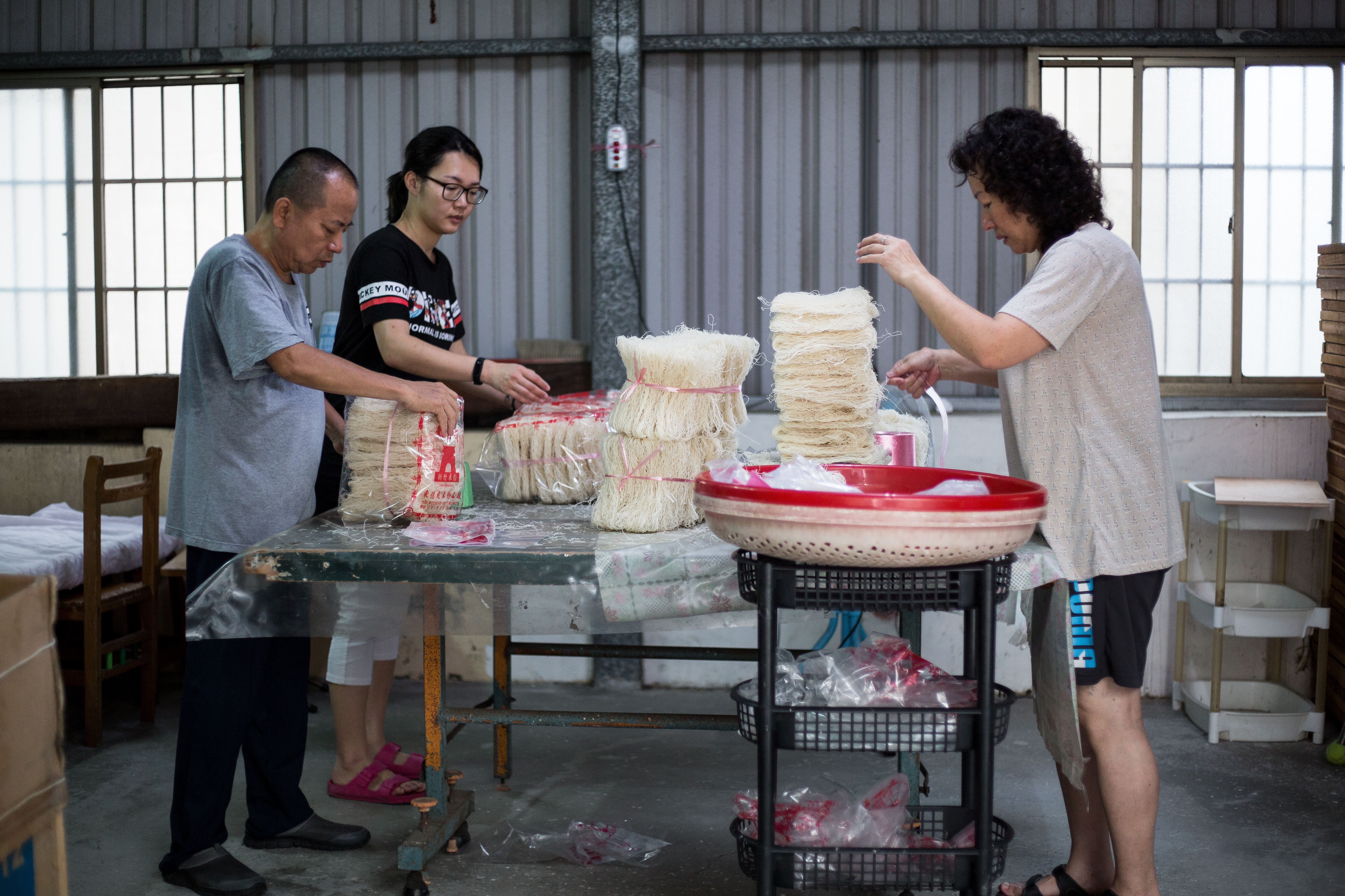 每天一大早，郭連進（左起）會率領媳婦陳宣媛與妻子林美津，會將前一天烘乾或曬乾的米粉秤重包裝。