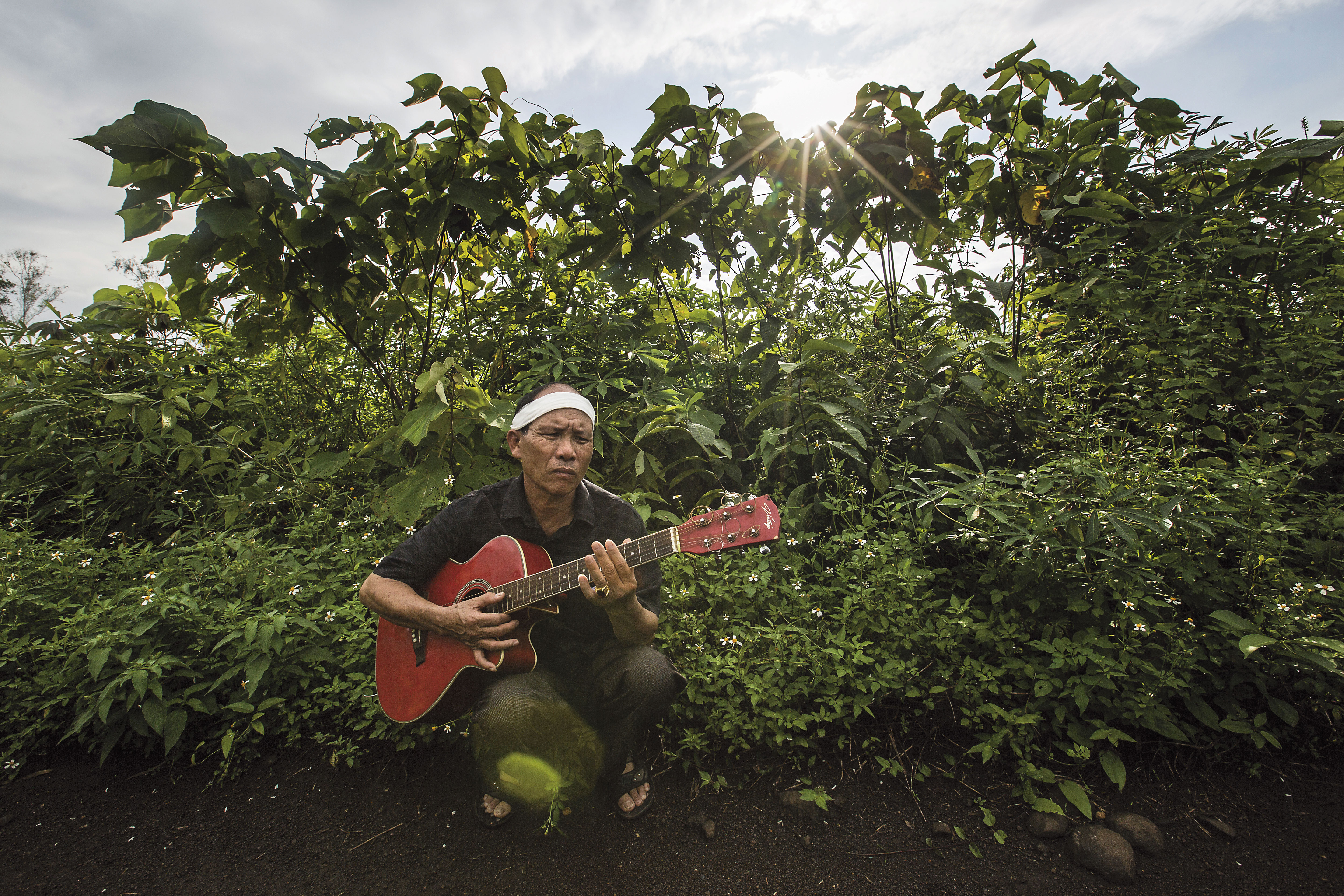 抱著阮國非生前最愛的吉他，站在準備給他養牛的土地前，父親阮國同心中有無限悲傷。