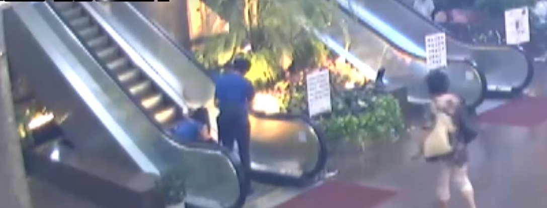 女童腳後跟被卡在電扶梯縫隙中，母親作勢幫忙拔出。（翻攝畫面）