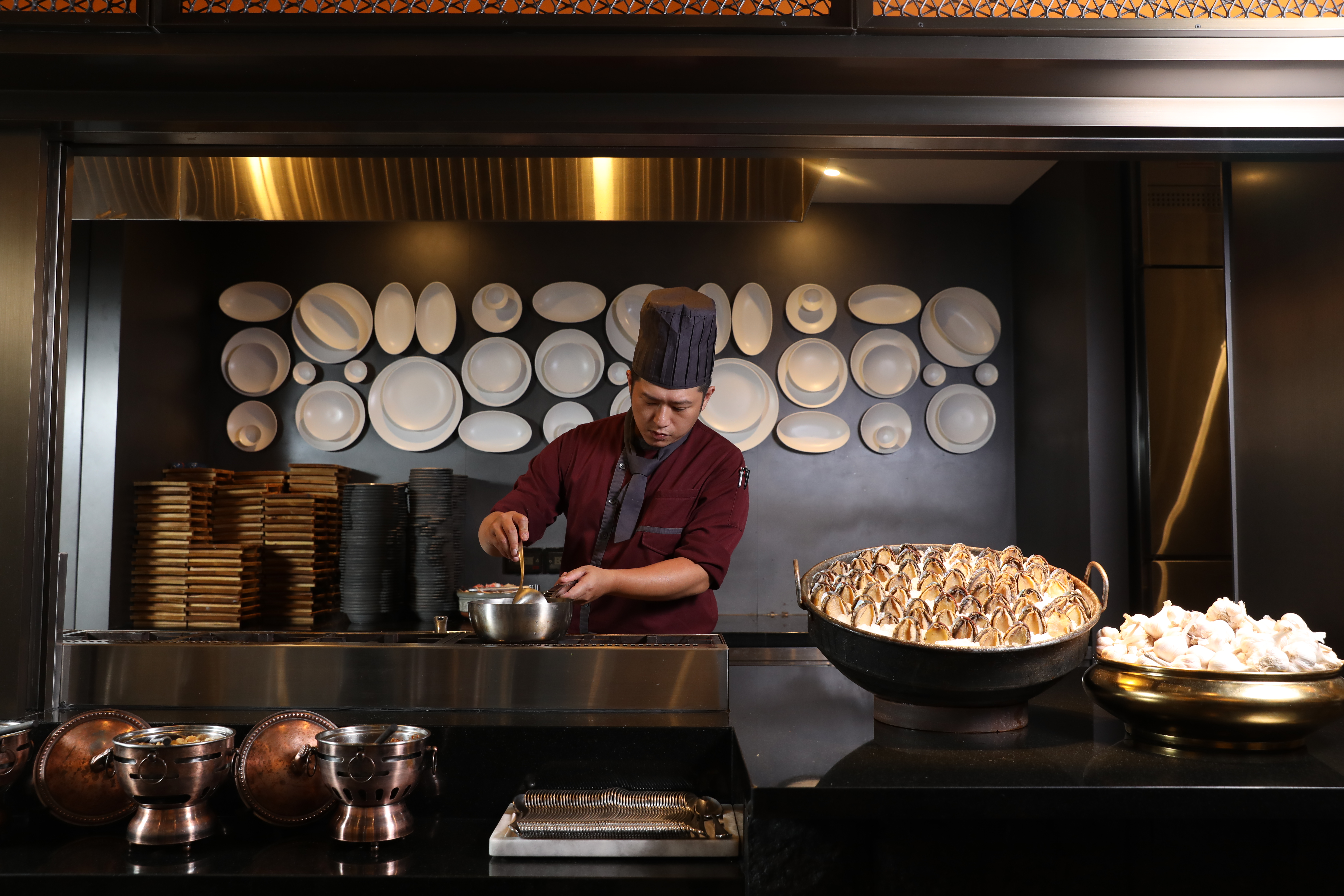 「INPARADISE饗饗」中廚主廚羅鈞瀚正在現煮「鮑魚海鮮粥」，檯面上一大鍋鮑魚，令人垂涎。