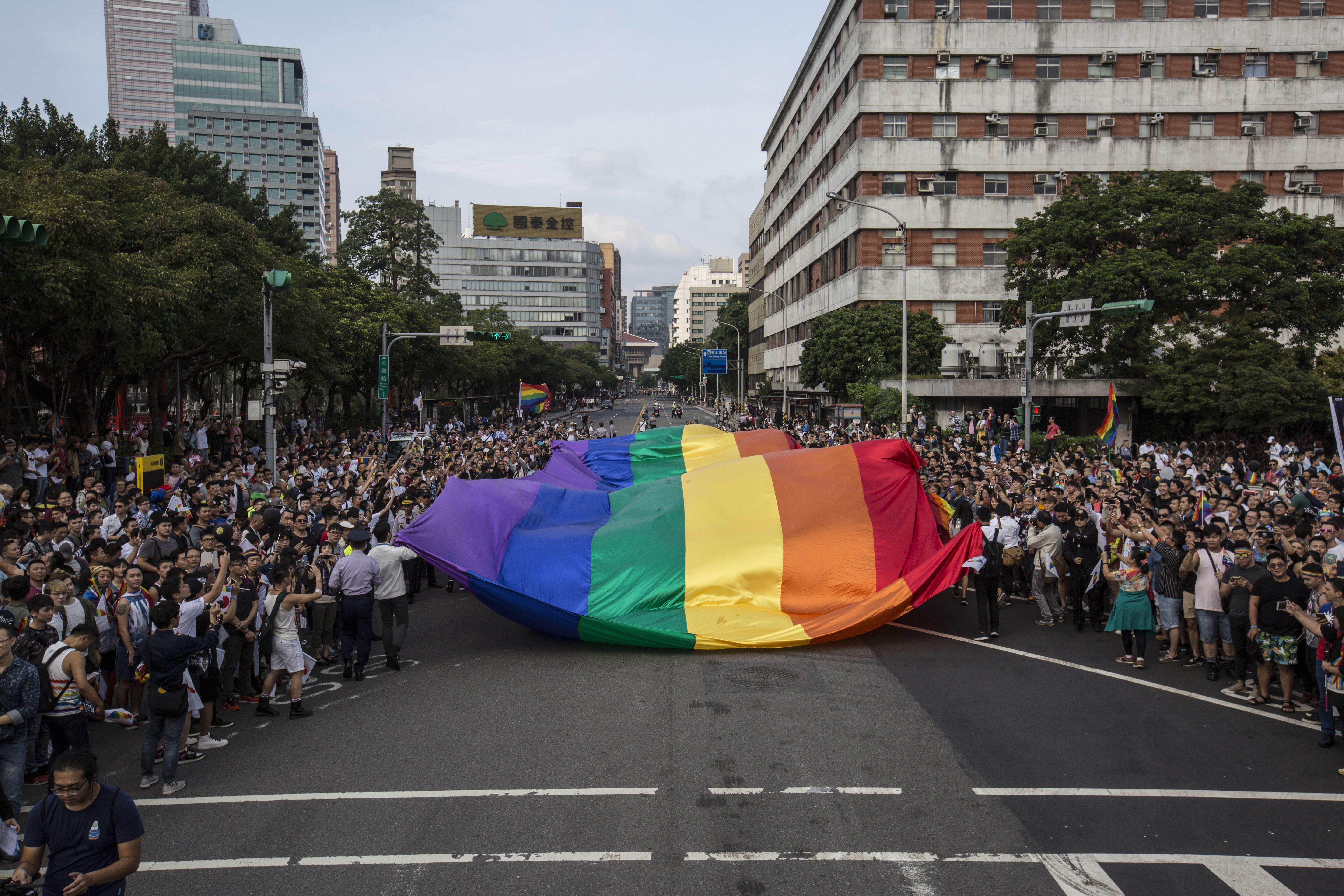 同志遊行開始前，由一大面的彩虹旗領頭往前走，道路兩旁都擠滿參與遊行的民眾。