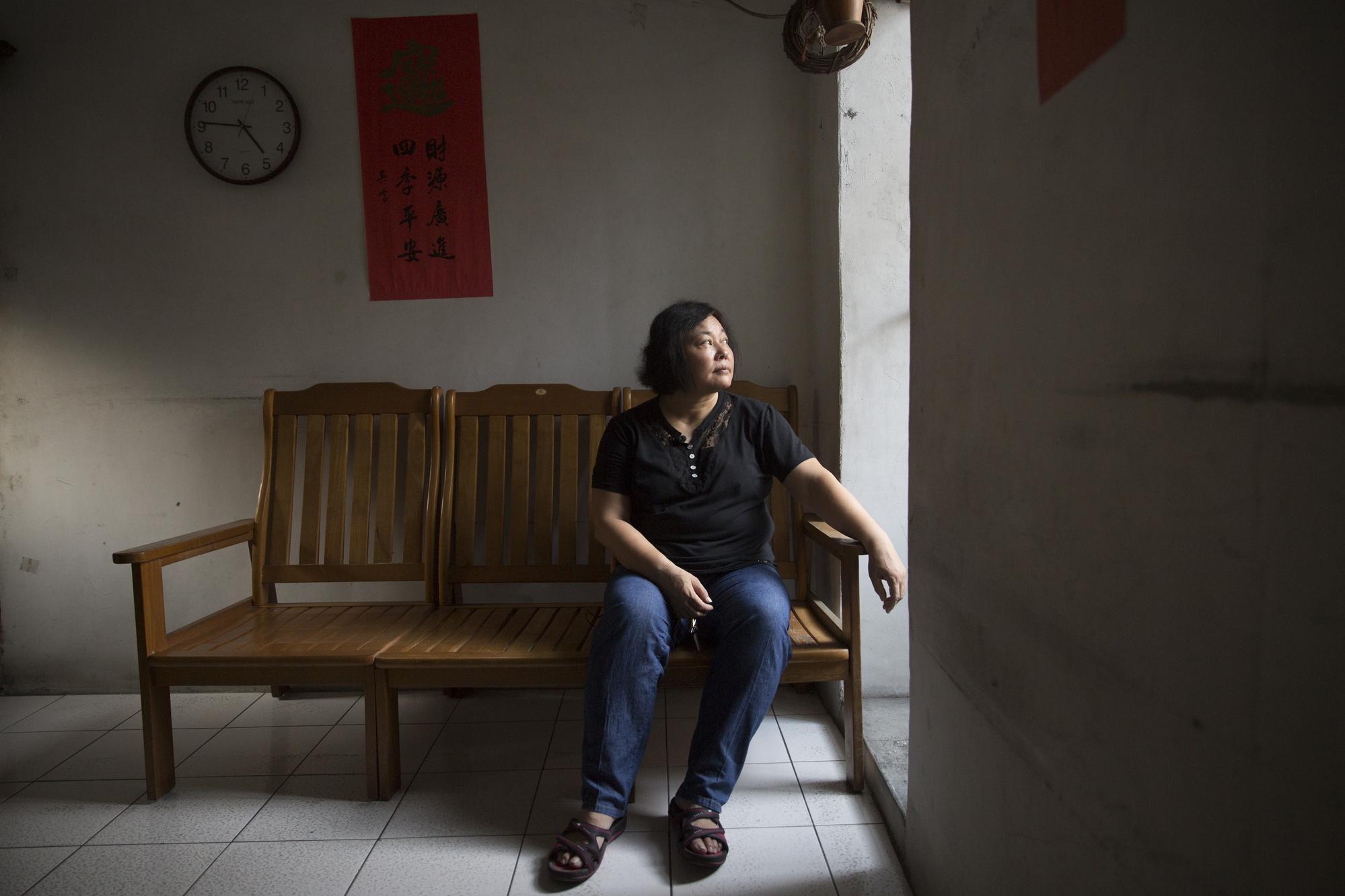 王淑芳坐在老家客廳，這是三兄妹從小到大生長的地方，如今多處漏水、裸露鋼筋，只留下佛堂與狗。
