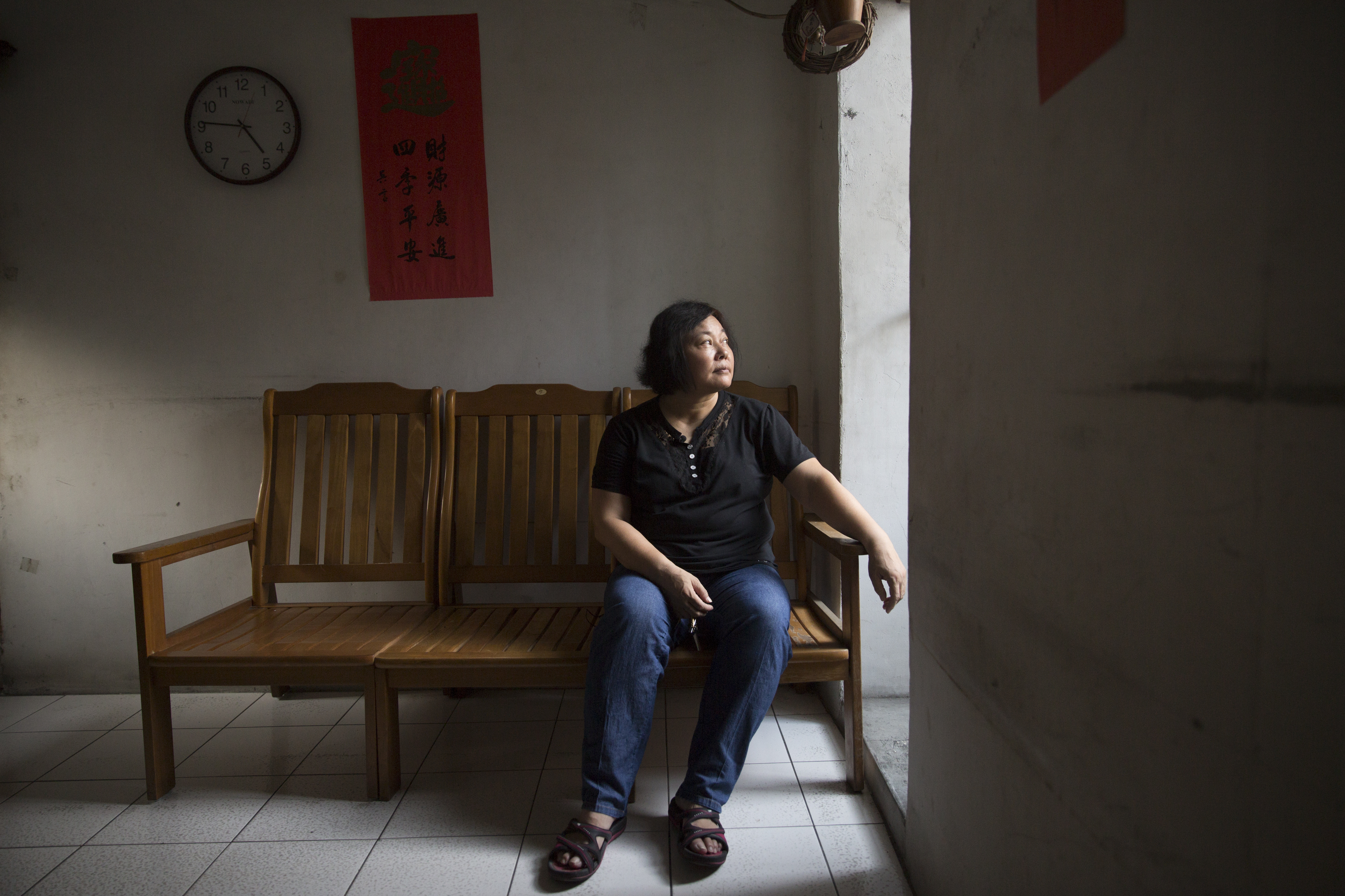 王淑芳坐在老家客廳，這是三兄妹從小到大生長的地方，如今多處漏水、裸露鋼筋，只留下佛堂與狗。