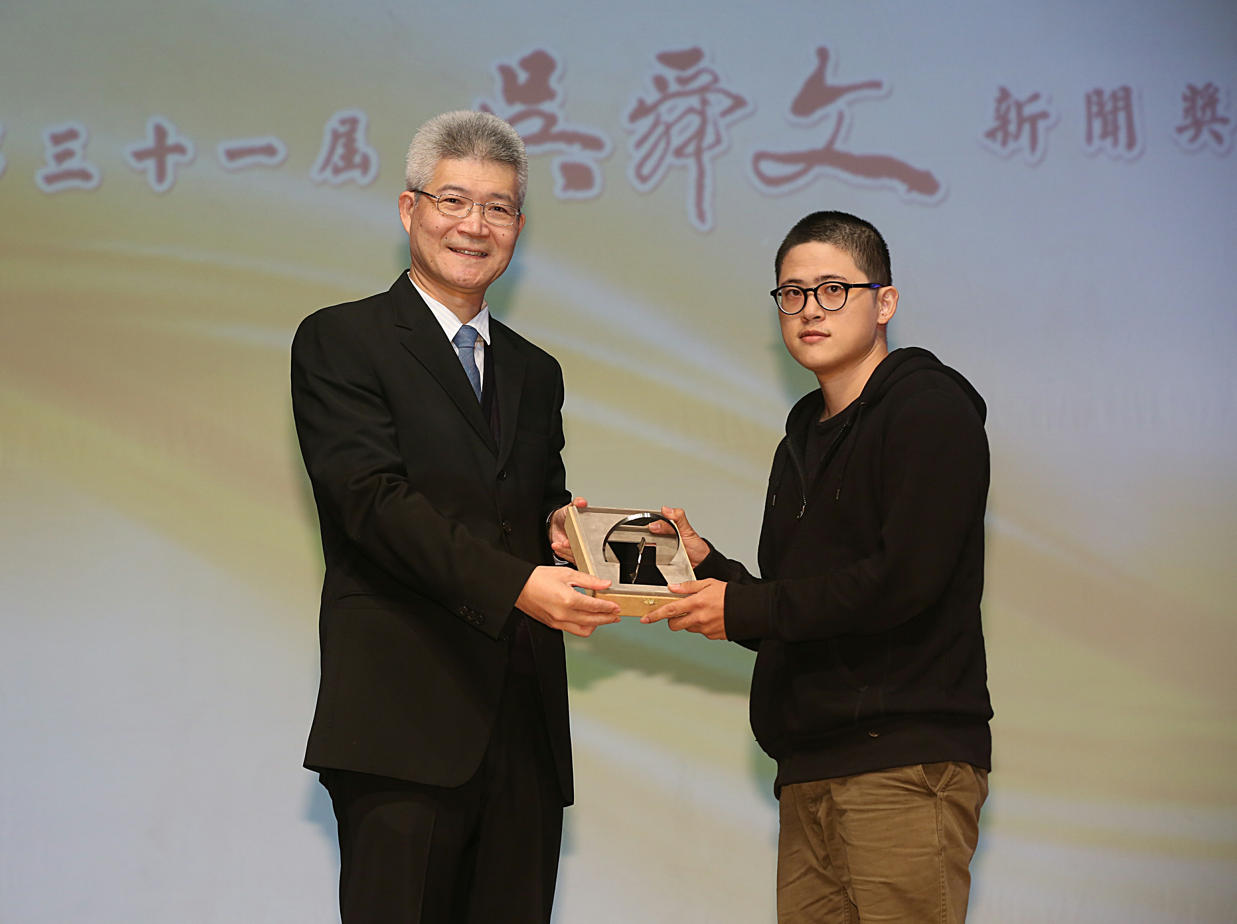 攝影記者楊子磊（右）以拍攝祈家威〈一個人的革命〉作品，於第31屆吳舜文新聞獎再度拿下單張新聞攝影首獎，並由大會評審團召集人胡元輝教授（左）頒發獎座。