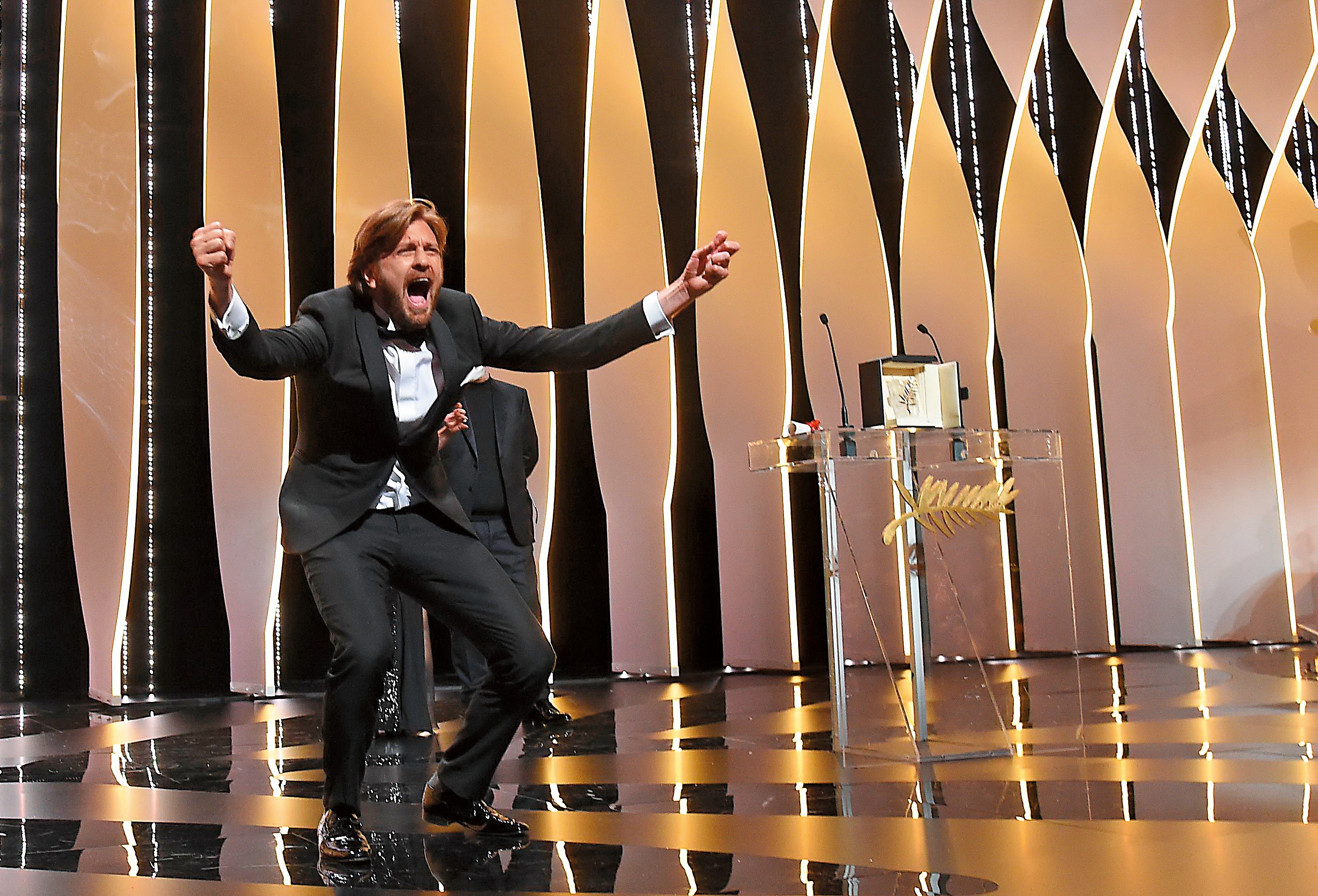  坎城影展頒獎典禮現場，魯本奧斯倫因摘下金棕櫚大獎開心耍寶。（東方IC）