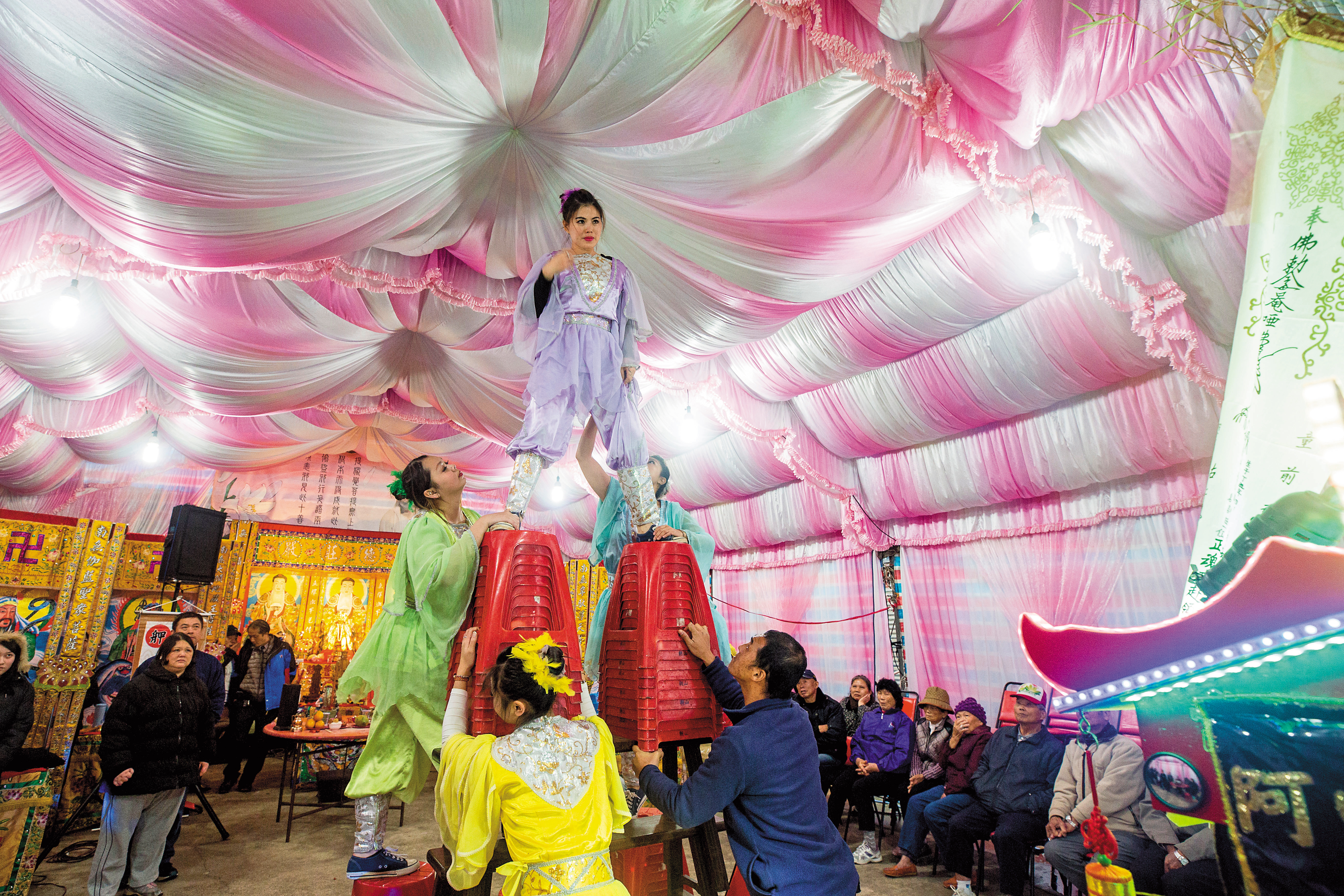 劉君玲爬到3公尺高的椅子上，下腰咬錢，是牽亡魂陣儀式特有的花招。