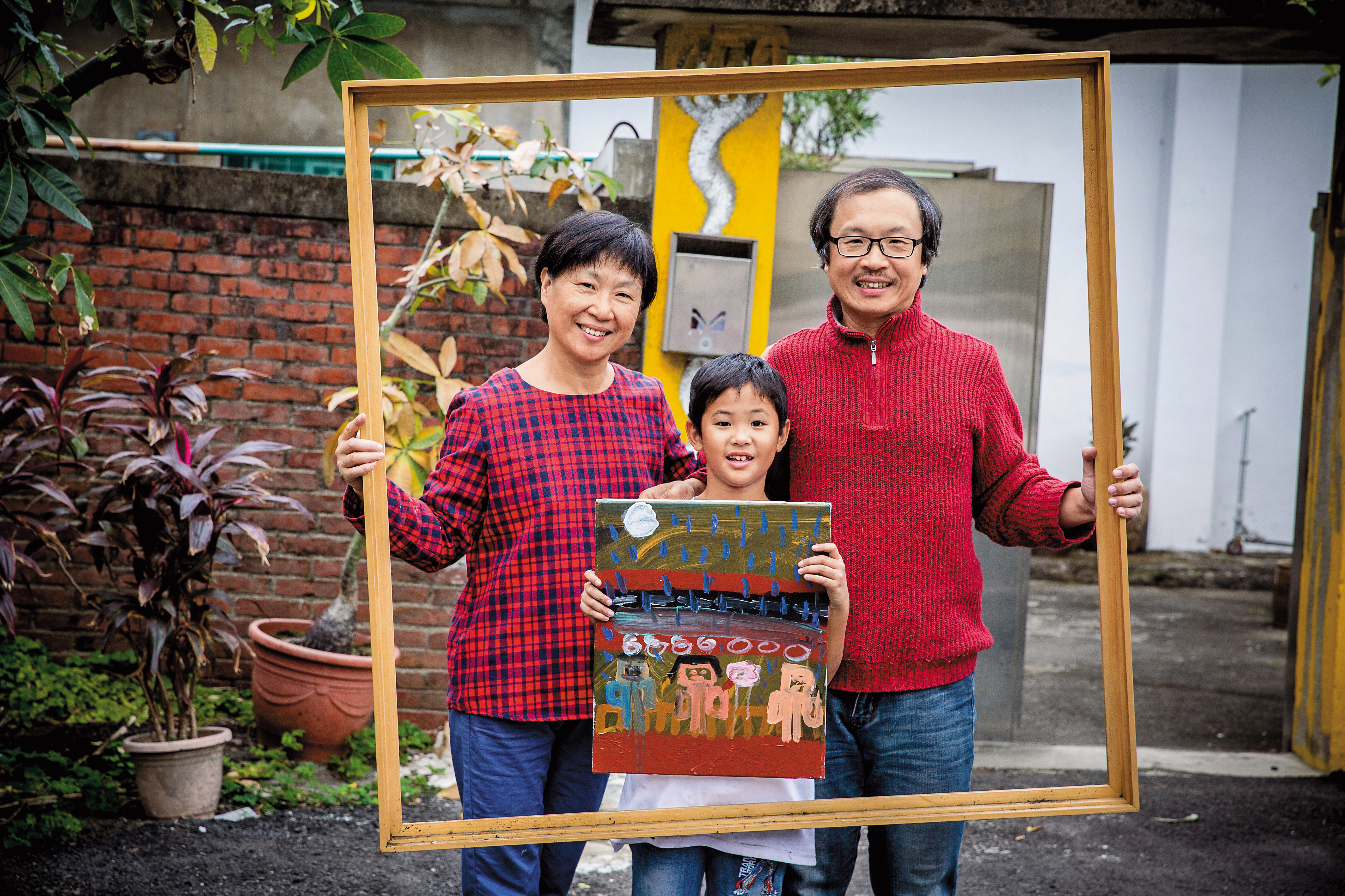 張立曄（右）曾是個鬱鬱少年，妻子朱鳳玲（左）與兒子小安（中）滋養他的正面能量。小安拿著自己畫的全家福。