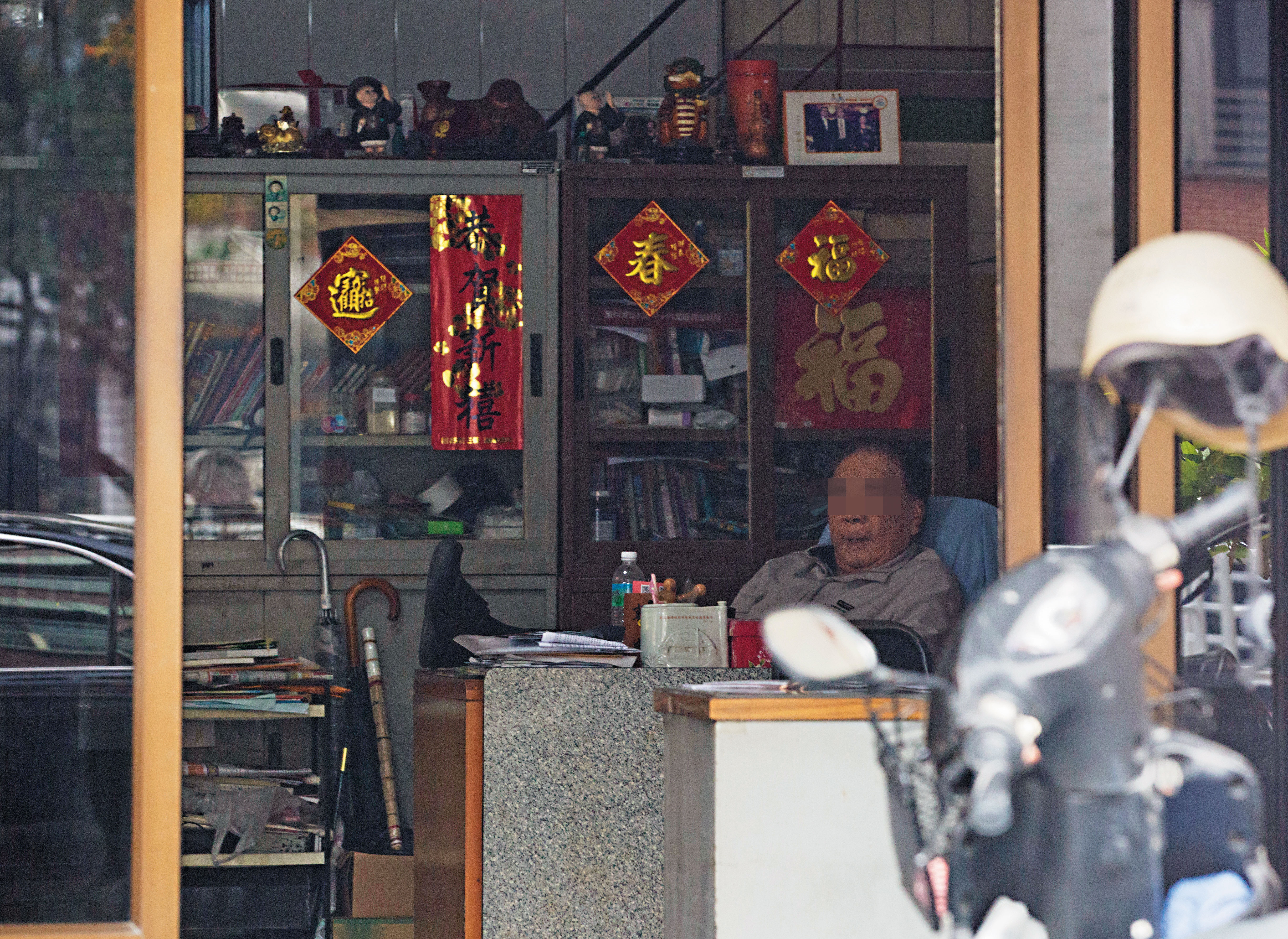 本刊走訪遠距中心得標廠商，外觀是一般民宅，從外向看內，沒有員工辦公，只有1名長者在辦公桌前打瞌睡。