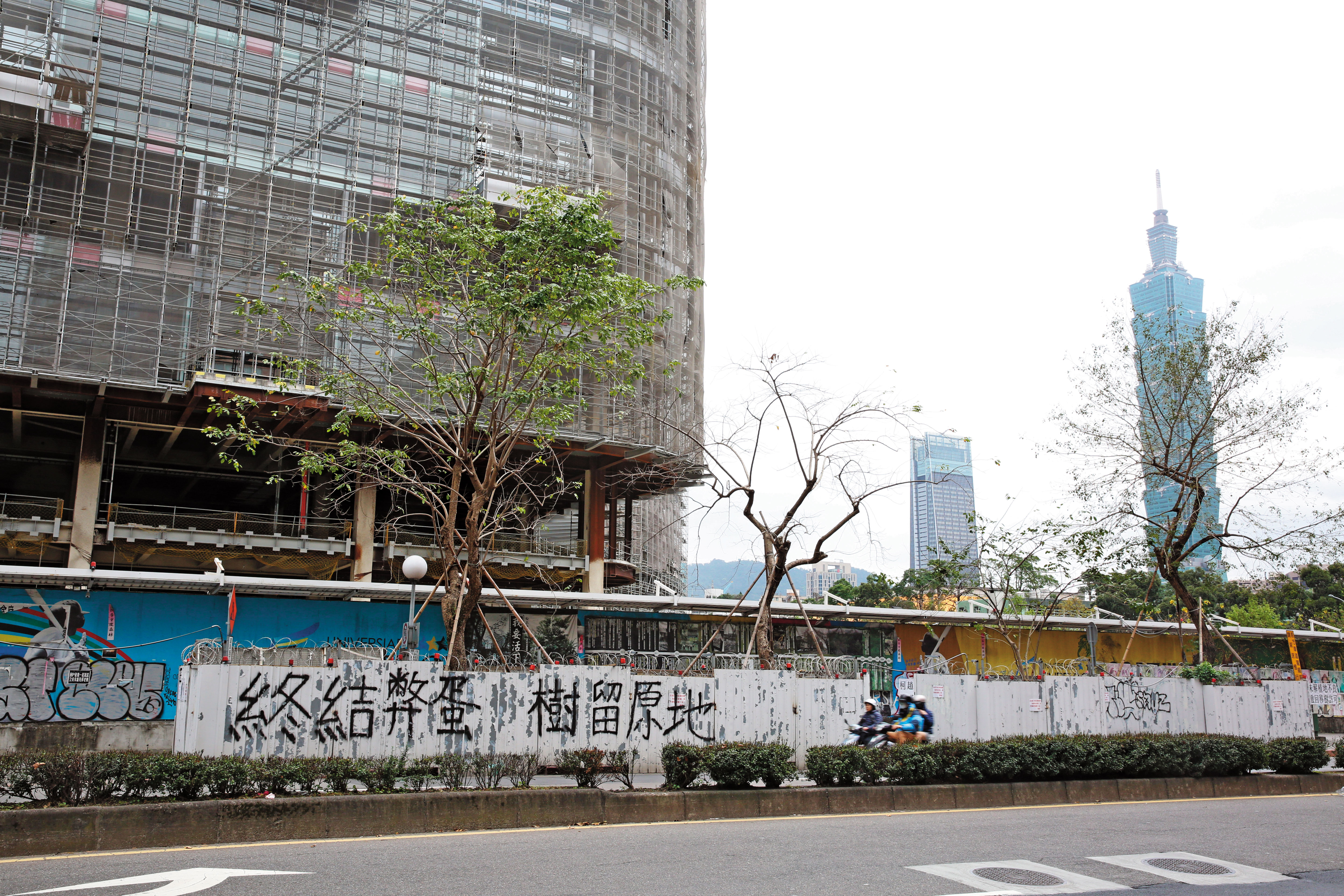 大巨蛋圍籬外牆遭反巨蛋的護樹團體懸掛布條抗議,柯團隊也擔心,讓大巨蛋復工超車,恐不利選情。