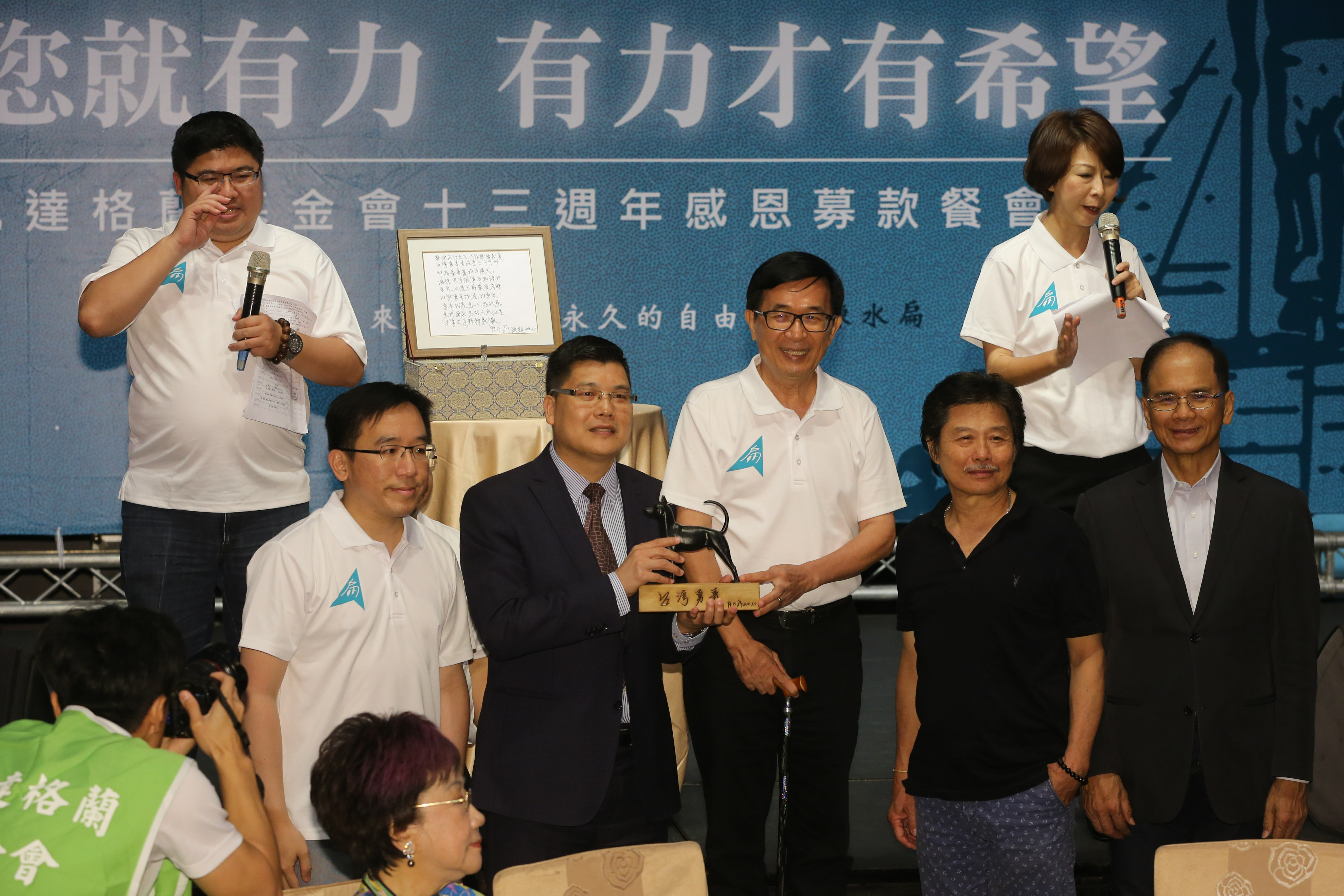 陳水扁以站在舞台前的墊箱手持麥克風介紹義賣品方式，技術性演說。