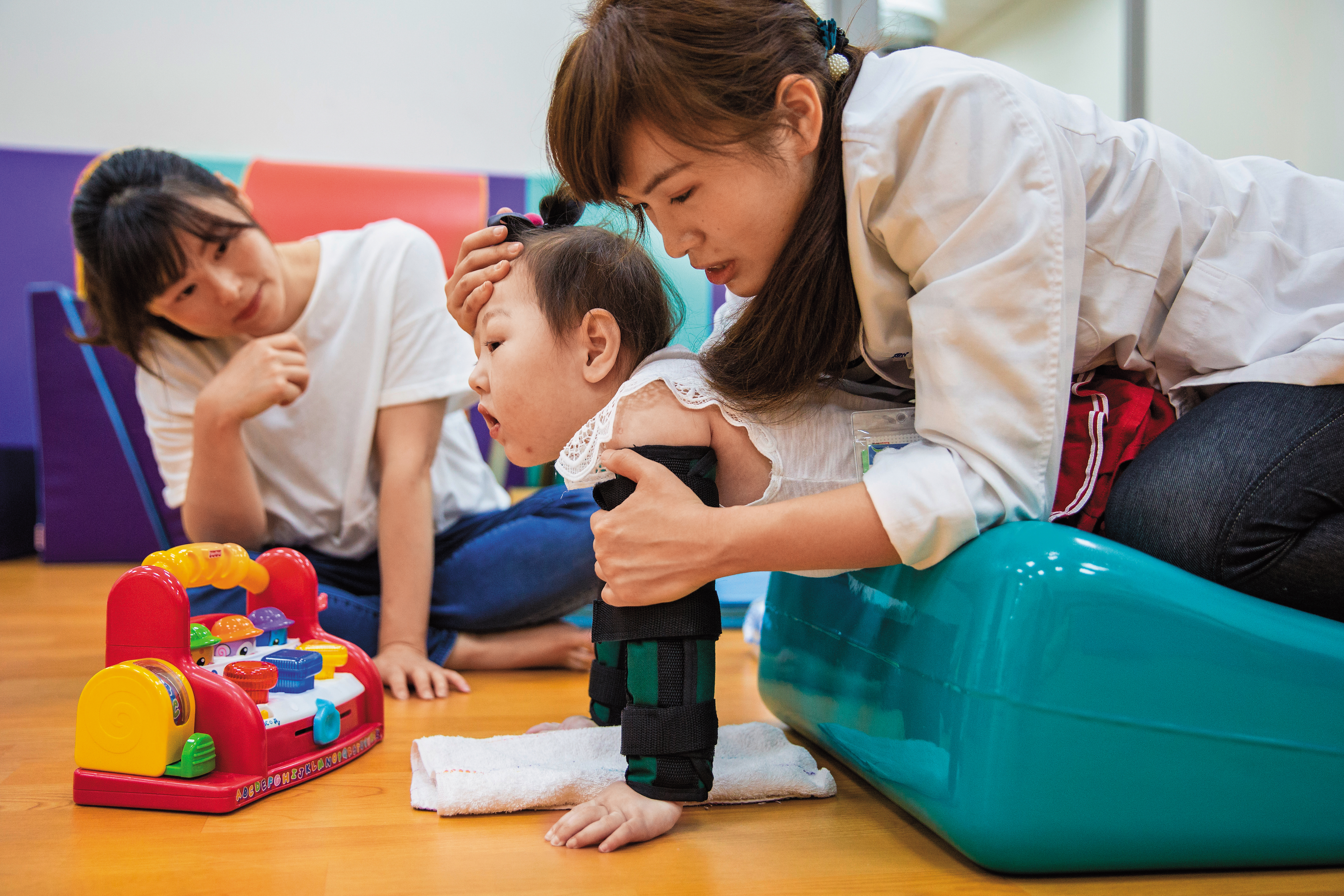 除了每天4次固定服藥、拍痰等，吳依凡（左）每週帶林芊羽（中）復健3次，在復健師的引導下，林芊羽會努力抬頭，讓媽媽也覺得欣慰。