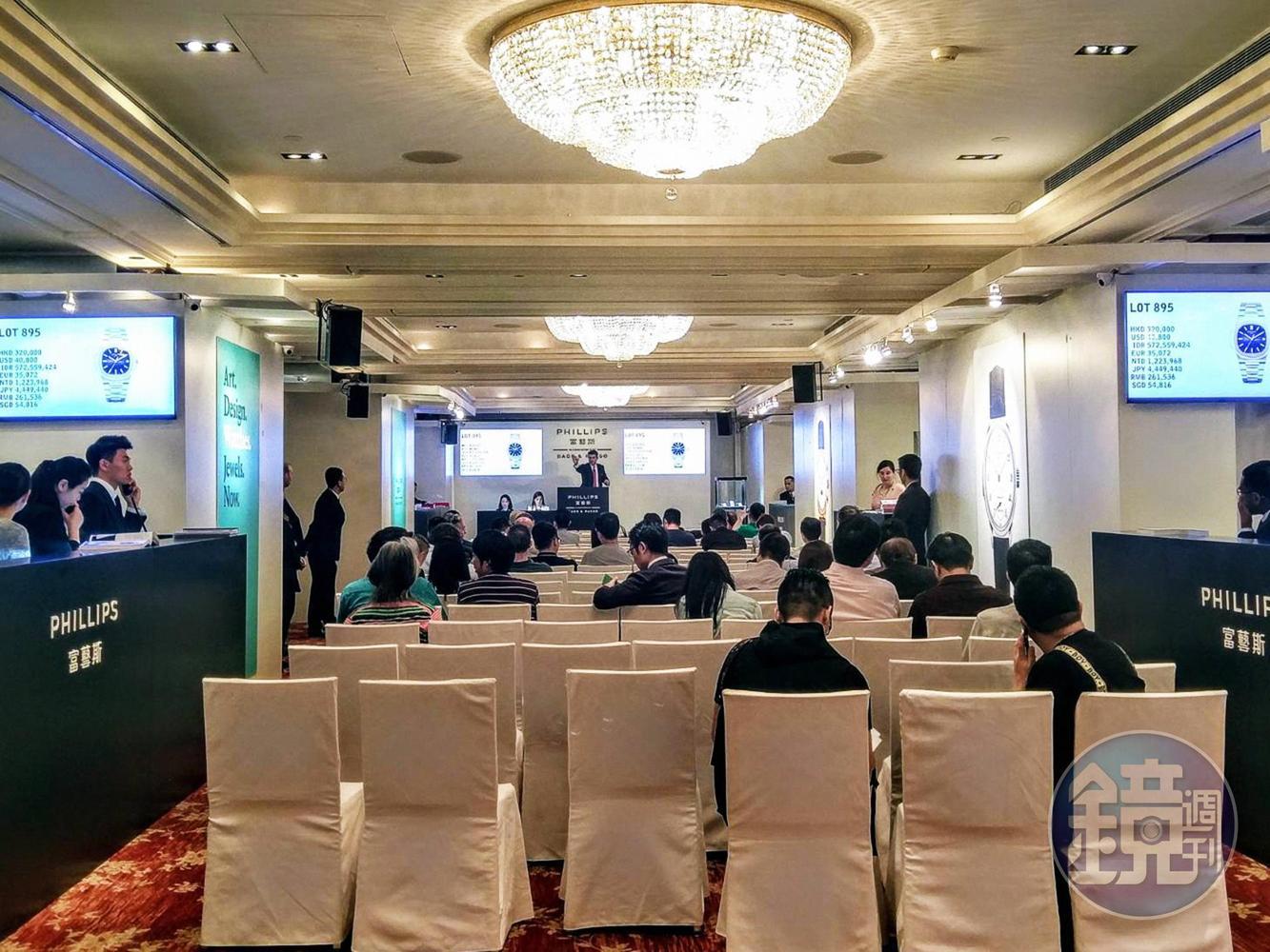 拍賣場為狹長形空間，至少可容納1、2百位競標者。正前方為拍賣官席，兩側則是負責接聽來自四面八方、代為以電話競標的鐘錶專家。