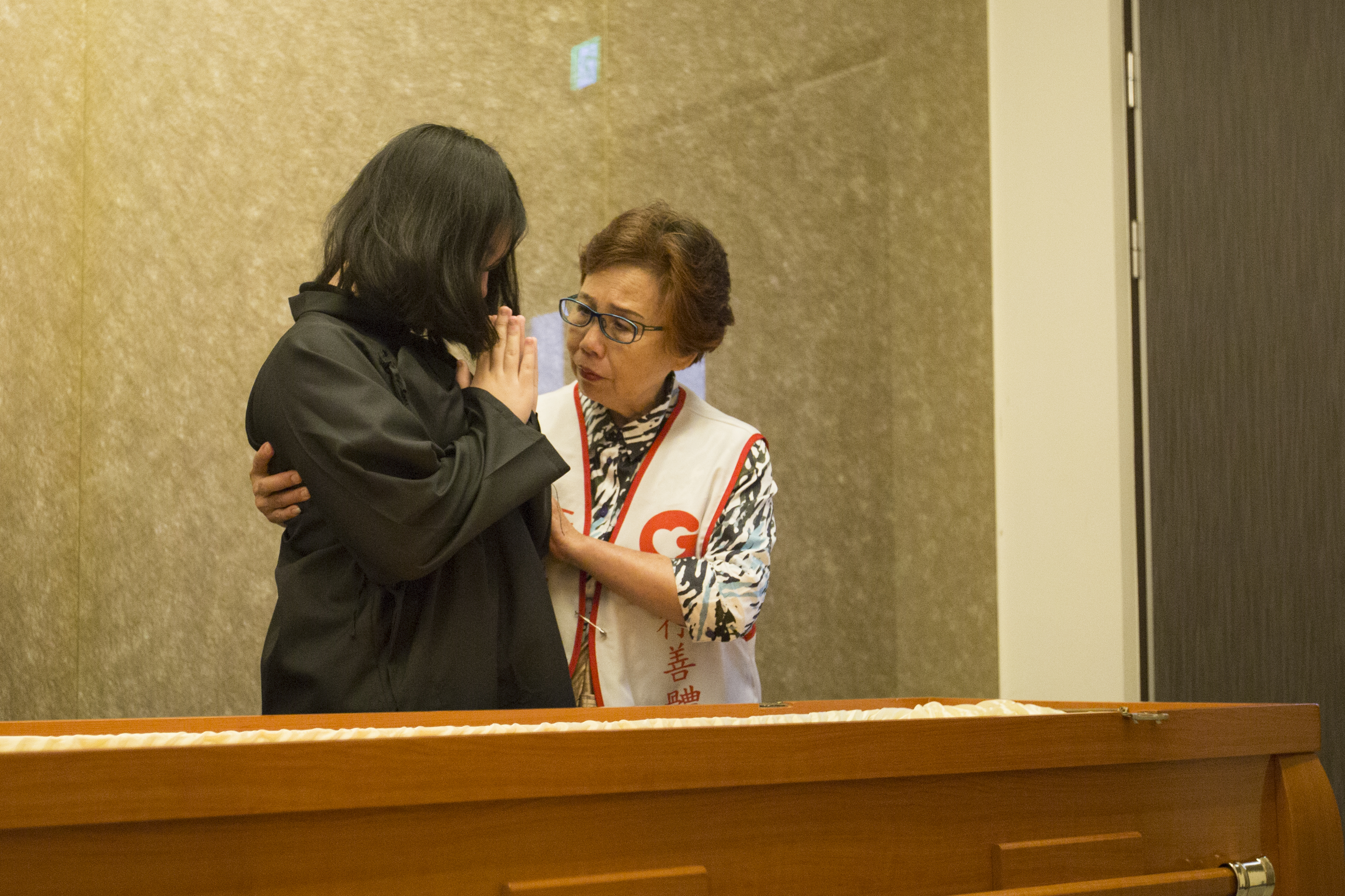 吳倪冬月（右）是善願愛心協會負責殮葬個案規劃的志工，那天，她陪著往生者的女兒瞻仰儀容，叨叨絮絮：「跟爸爸說再見，小心眼淚不要滴在爸爸身上……」