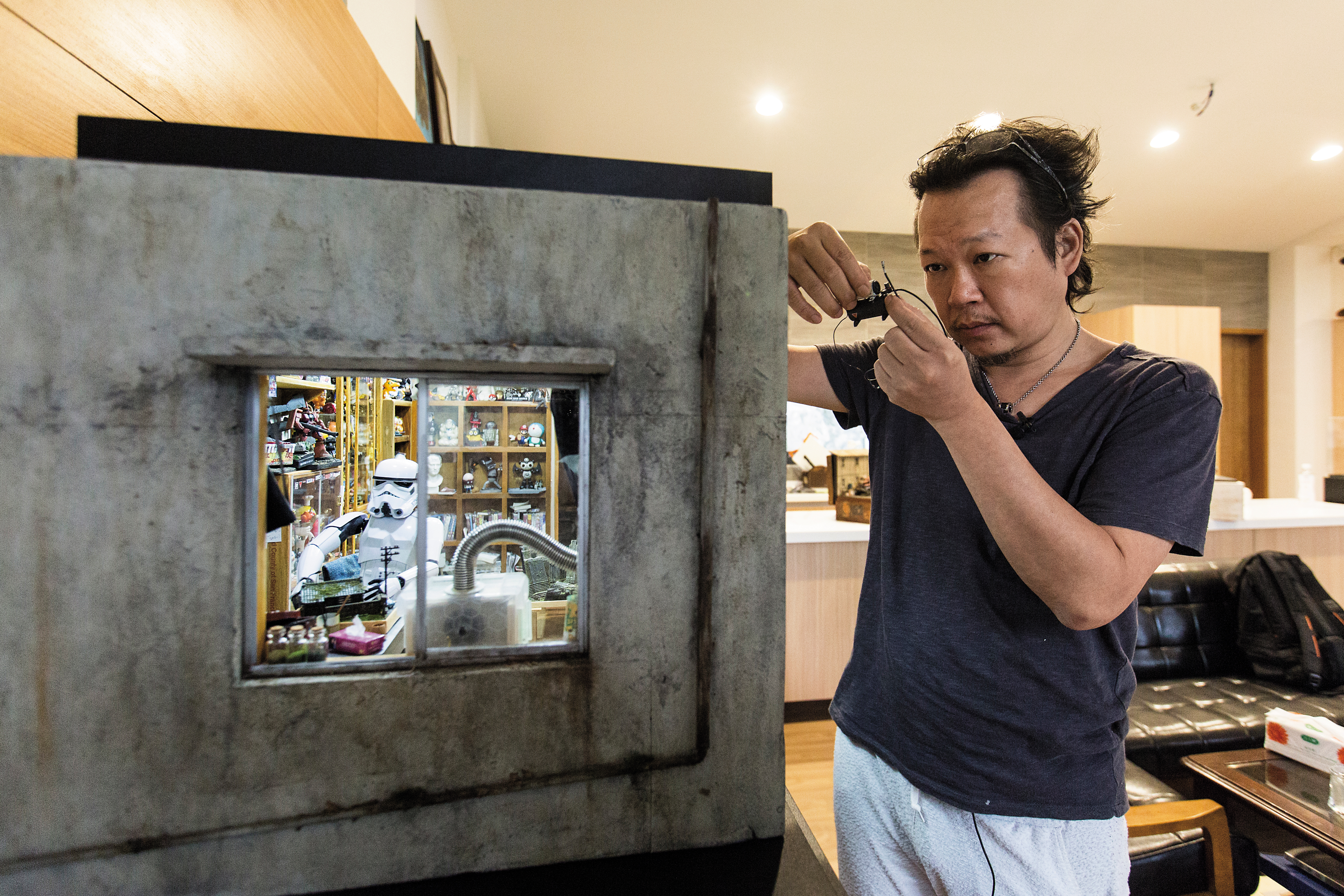 「宅男的房間」作品無實際場景參考，鄭鴻展說，平時靈感來源多來自日常生活及國外畫家的IG、臉書和插畫，他再思考把平面做成微縮模型的可能性。手上所持壓縮機為廢料製作。