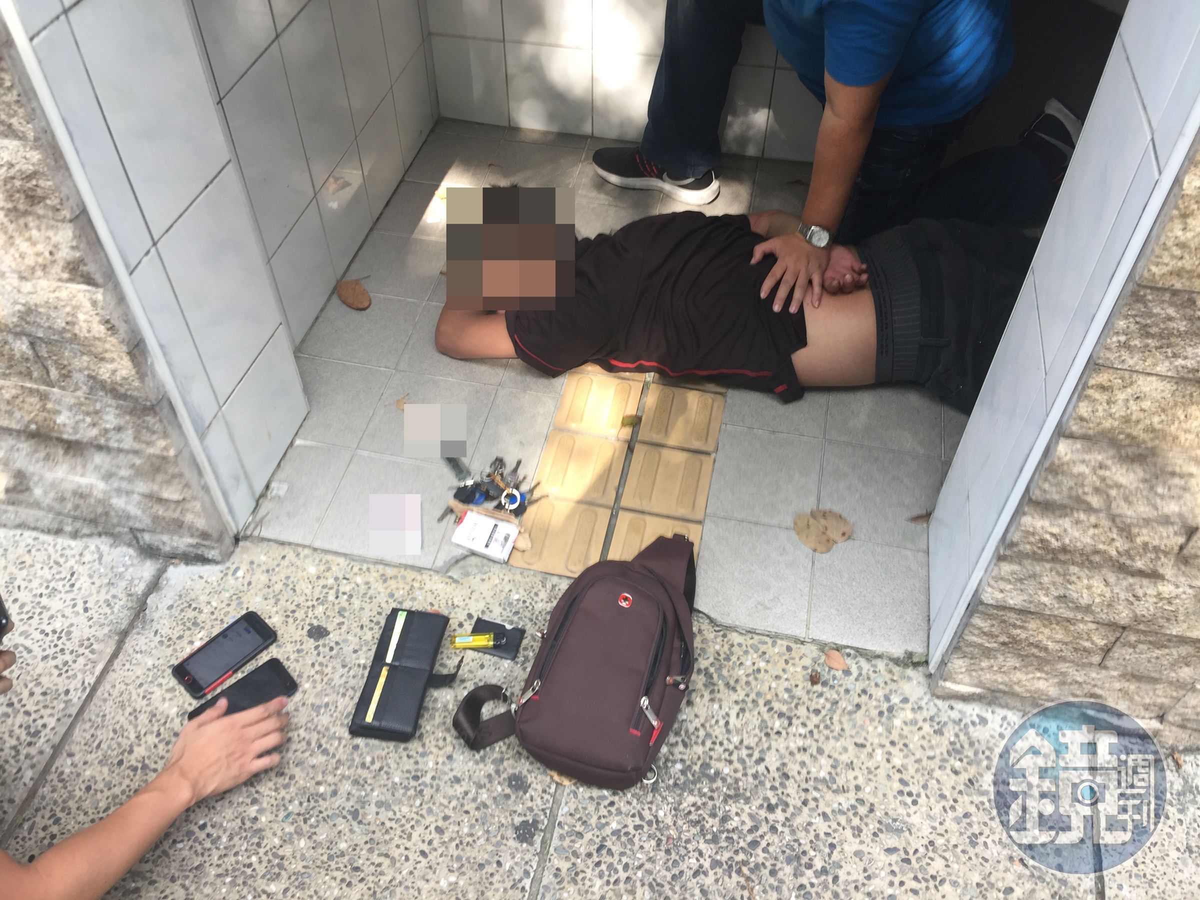 在廁所進行「死轉手」的詐騙集團成員被發現警方在他頭頂偷拍時，意圖搶奪警方手機遭警強押在地。（刑事局提供）