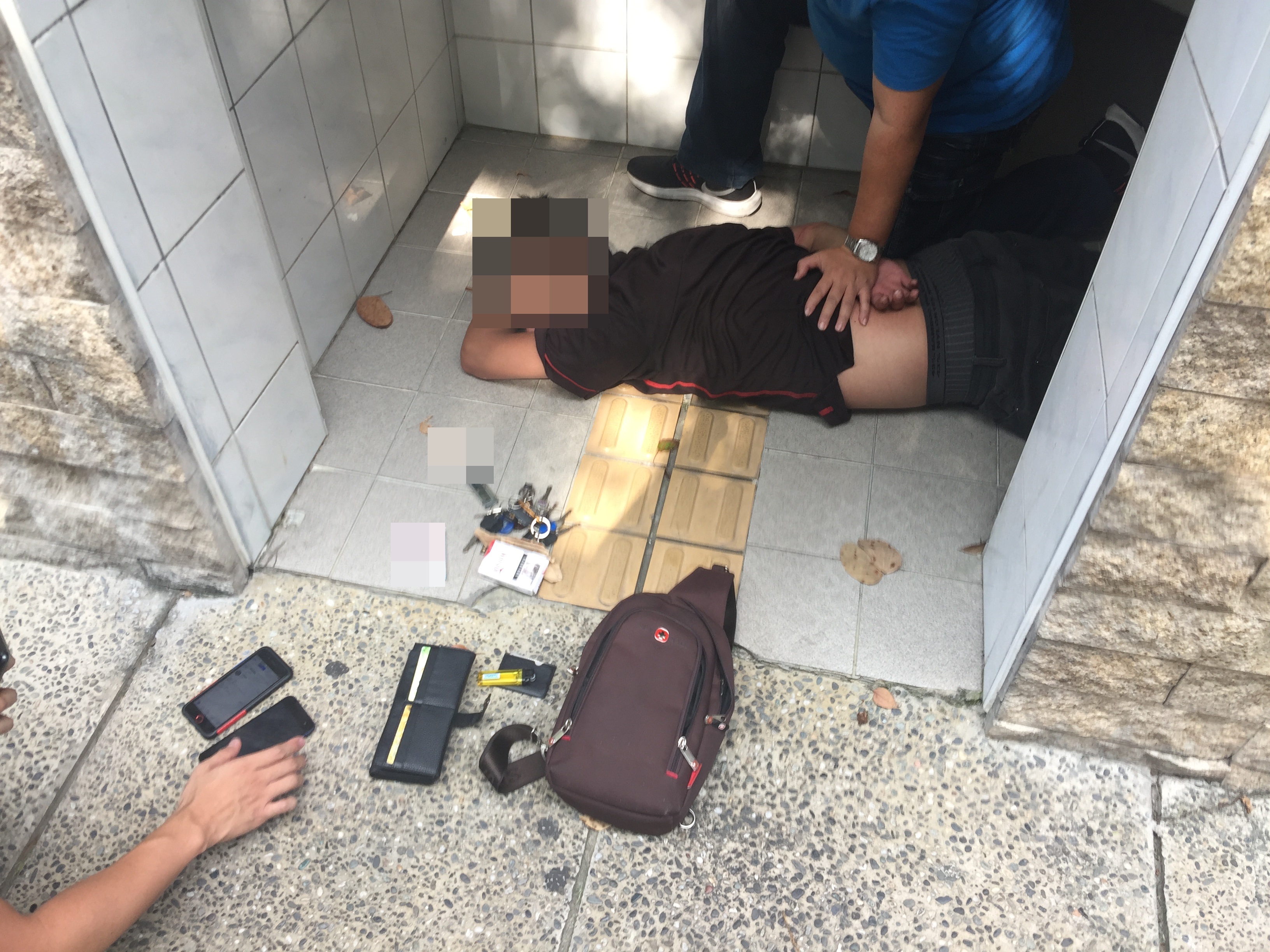 在廁所進行「死轉手」的詐騙集團成員被發現警方在他頭頂偷拍時，意圖搶奪警方手機遭警強押在地。（刑事局提供）