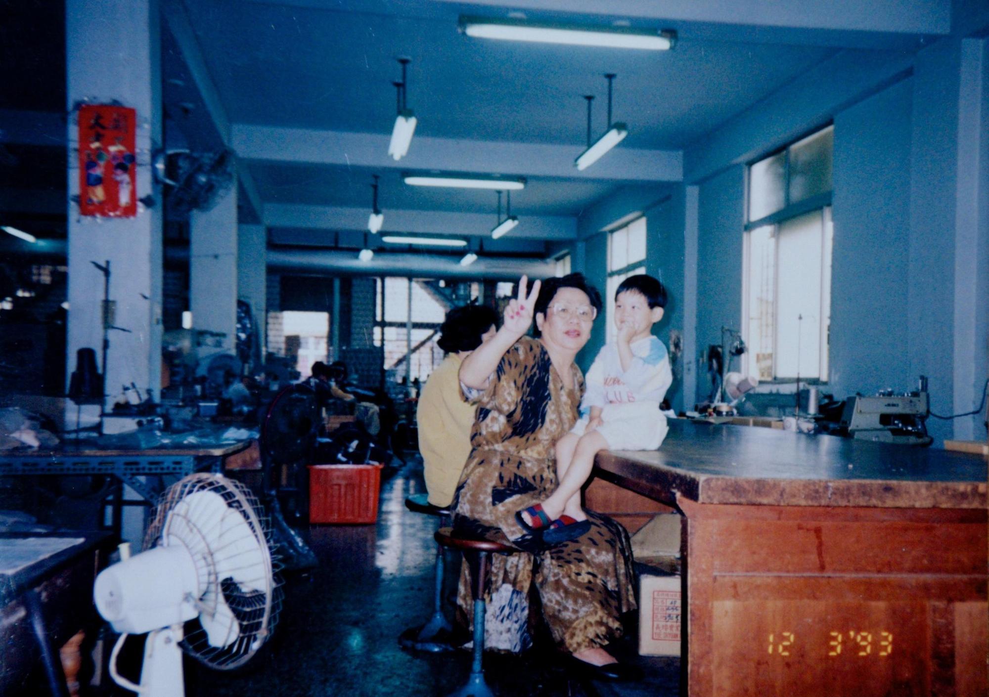 中美牌學生服第一代黃金（左）抱著第三代蔡旺達（右），在工廠內合影。（黃金提供）