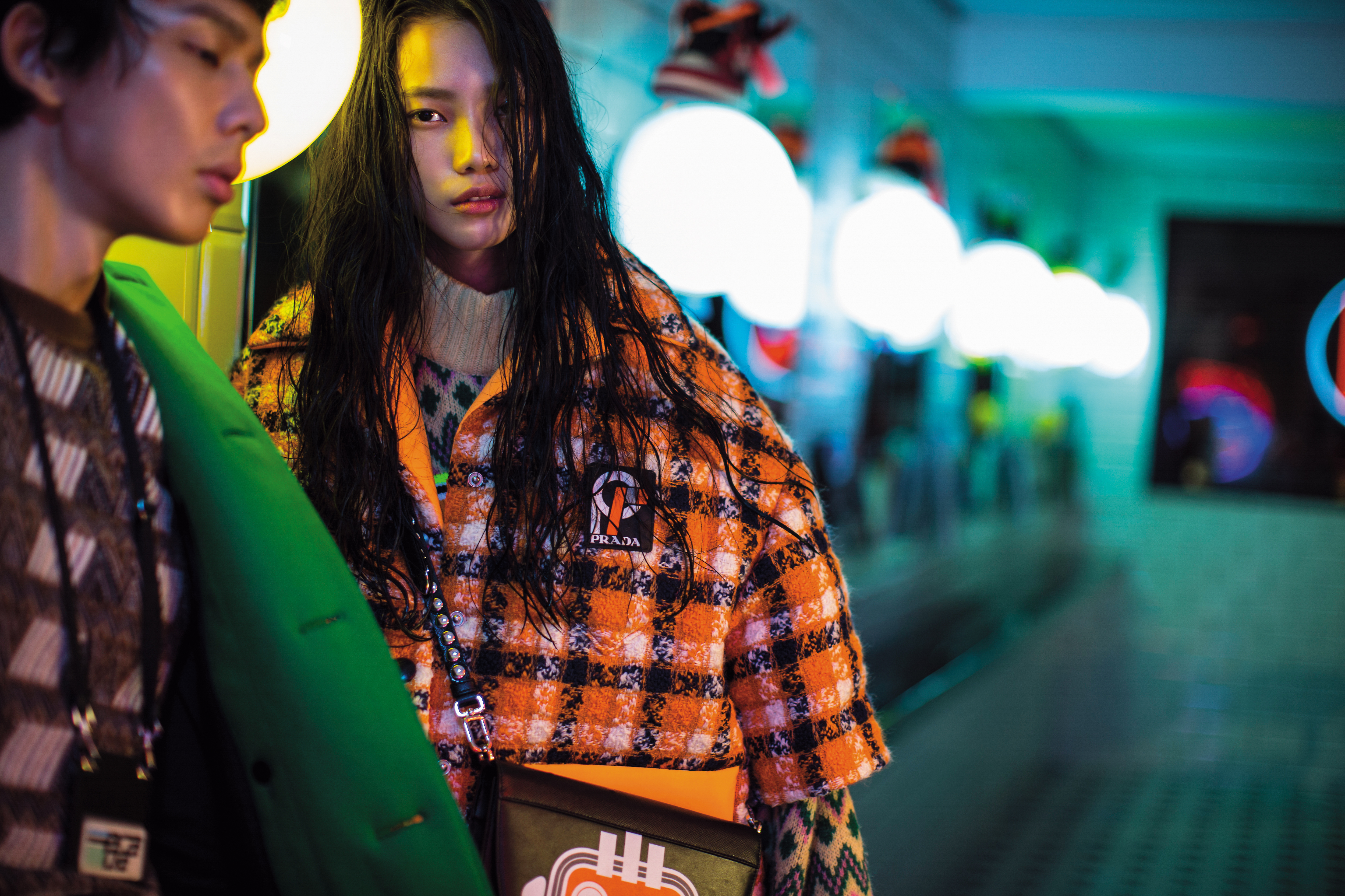 男，綠色大衣，NT$158,500／幾何圖紋V領針織衫，NT$33,000／工作證吊牌，NT$7,000。女，毛呢拼接尼龍格紋外套，NT$70,500／幾何圖紋針織衫，NT$35,500／機器人印花Elektra鉚釘肩背包，NT$73,500。（All by PRADA）