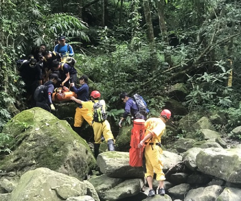 搜救人員翻越山谷，運送黃男夫婦下山治療。（消防局提供）
