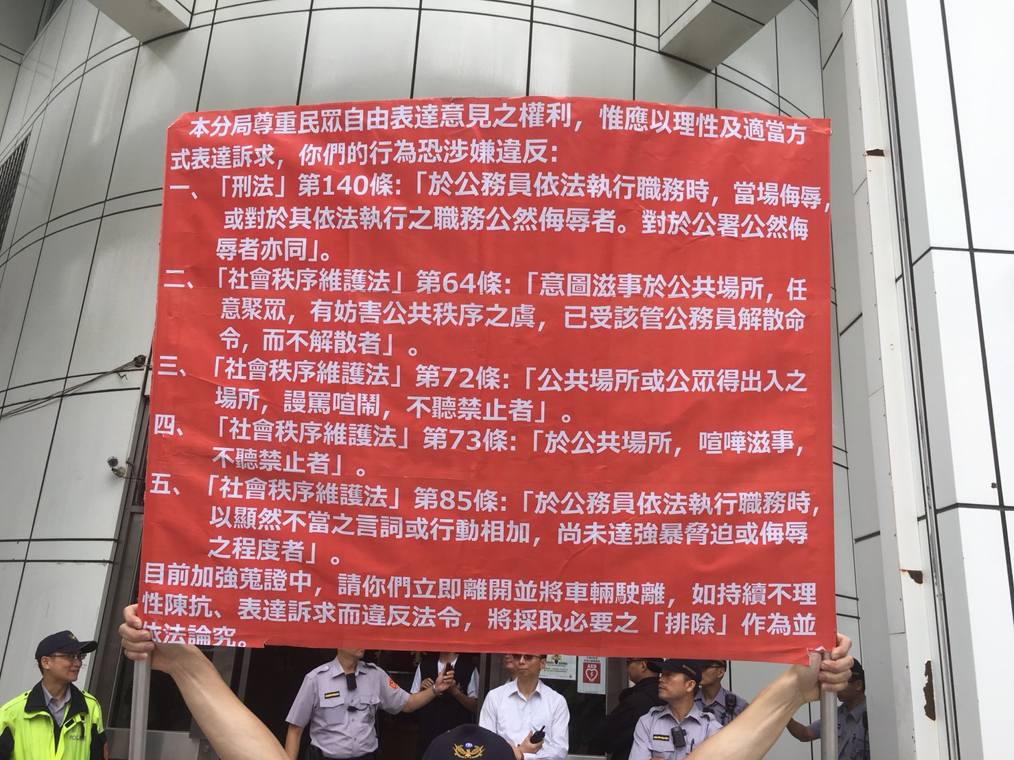 盧朝財等人聚眾抗議，警方舉牌告知違法。（翻攝畫面）