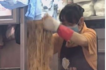 一名餐廳女員工以塑膠手套隔熱炒麵，被網友質疑可能釋出的化學物質。（翻攝自盡在元朗粉專）