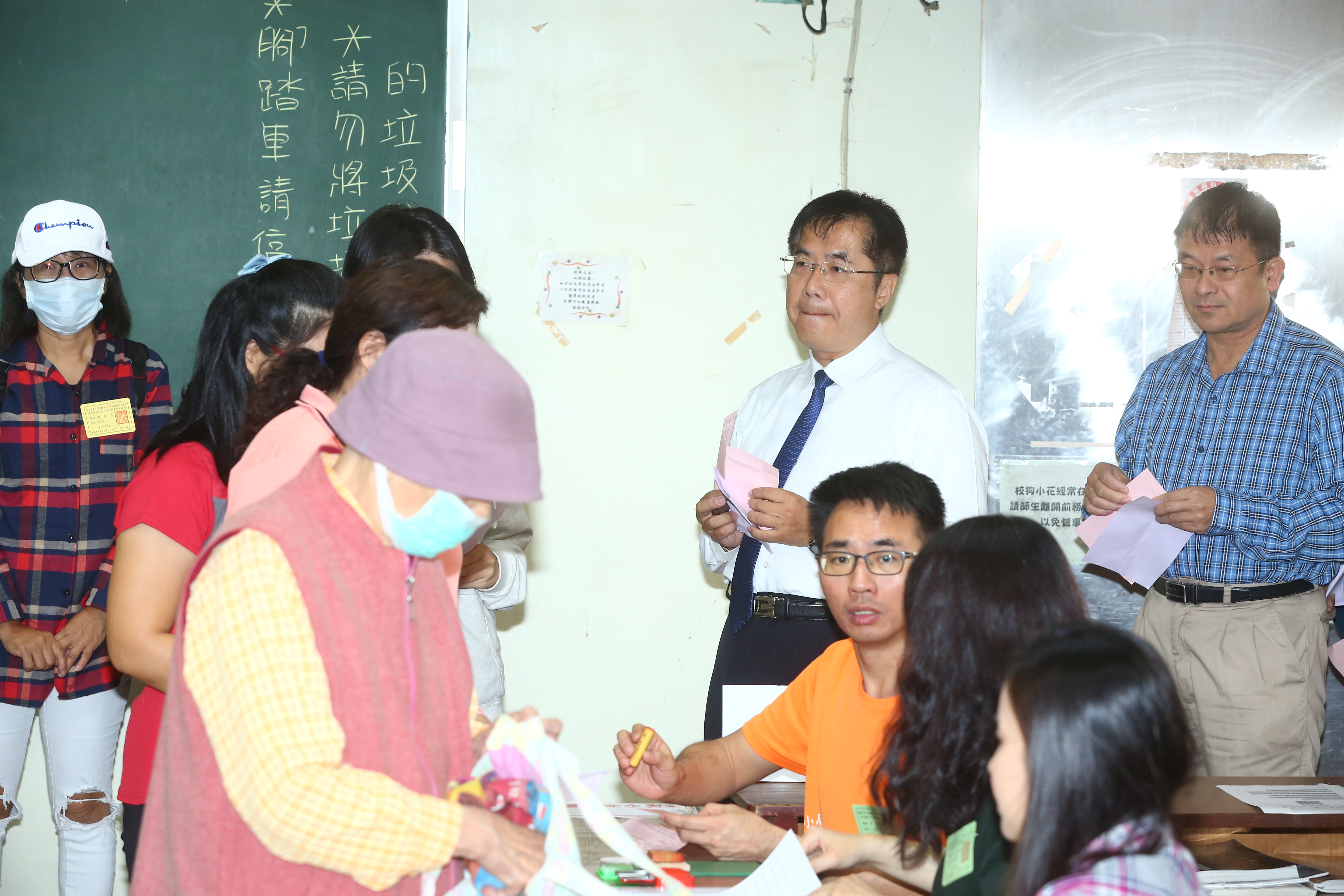 台南市長候選人黃偉哲攜帶投票通知單前往投票所，前方民眾正在領取選票。（王均峰攝影）
