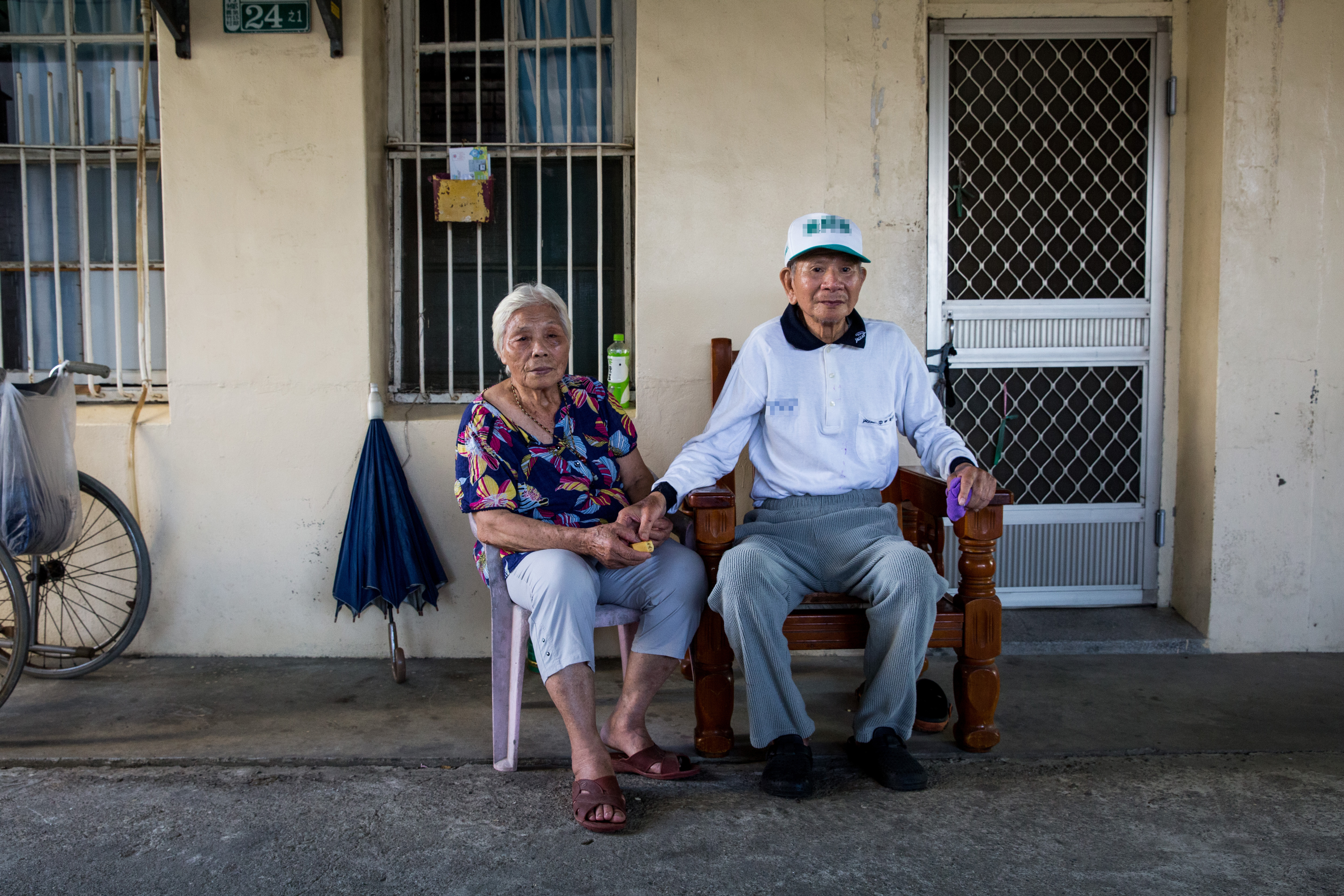 吳連珠（左）和翁興雄（右）在自家前門坐著休息。社工表示，能這樣坐著已非常不容易。