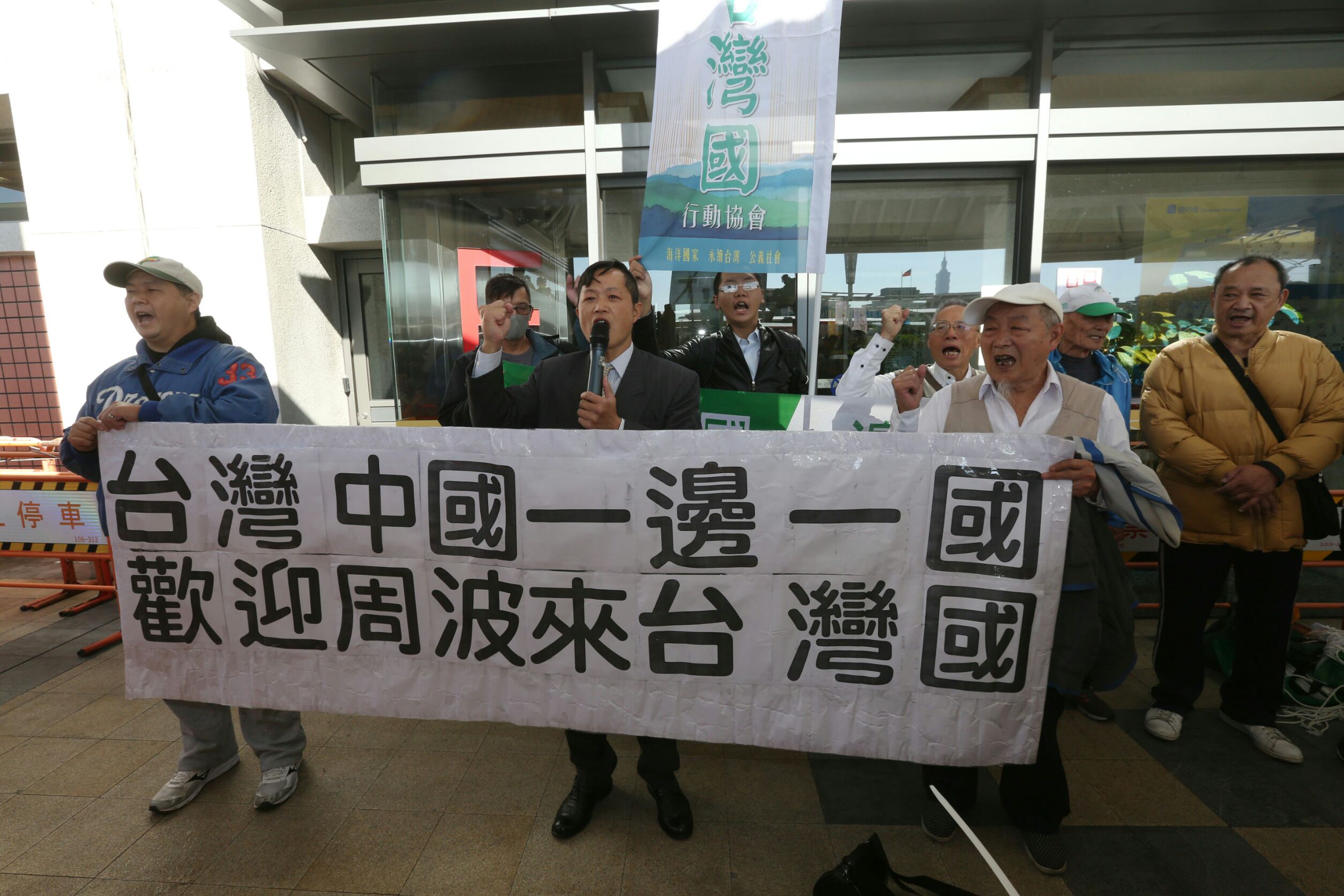 周波抵台後，出機場前碰到台灣國成員大喊高舉布條大喊「台灣中國一邊一國」。
