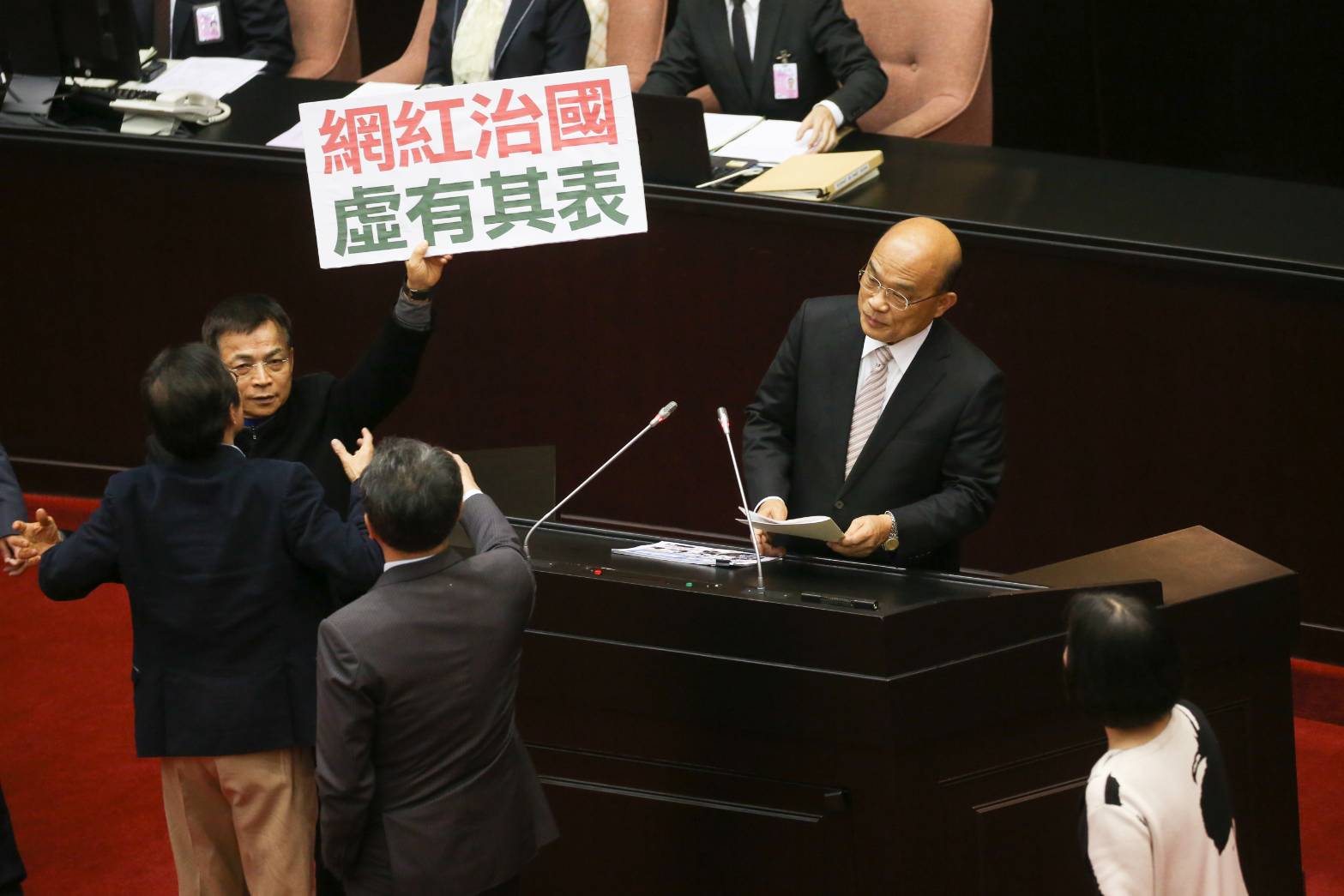 蘇貞昌上台報告時，國民黨立委賴士葆還是在他身旁舉著標語抗議。